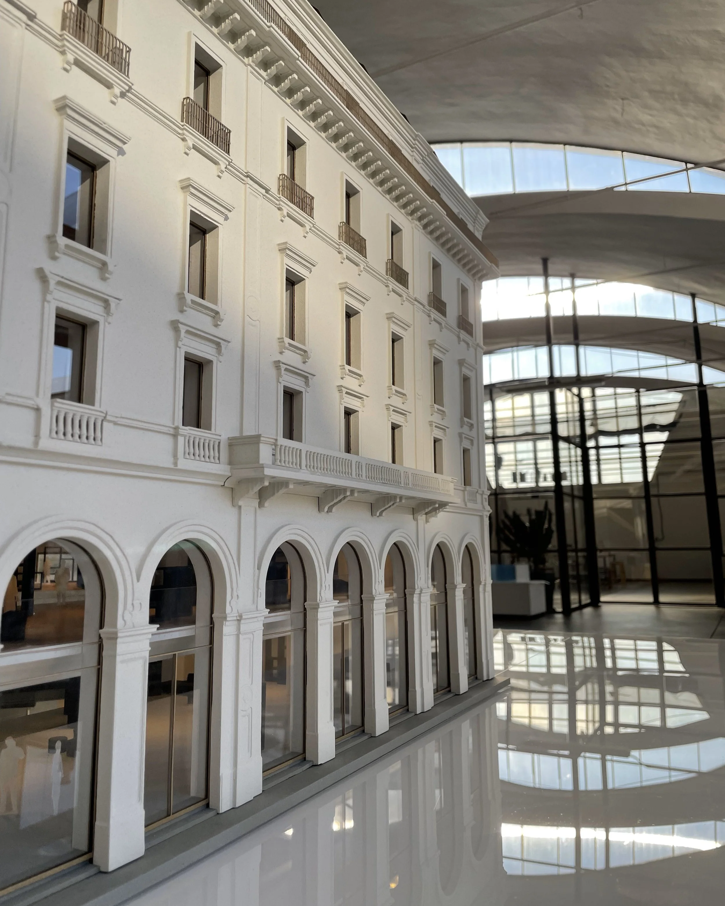 Modello di un edificio in stile classico con balconi e finestre e un grande spazio interno con soffitti curvi e ampie finestre, riflesso sul pavimento.