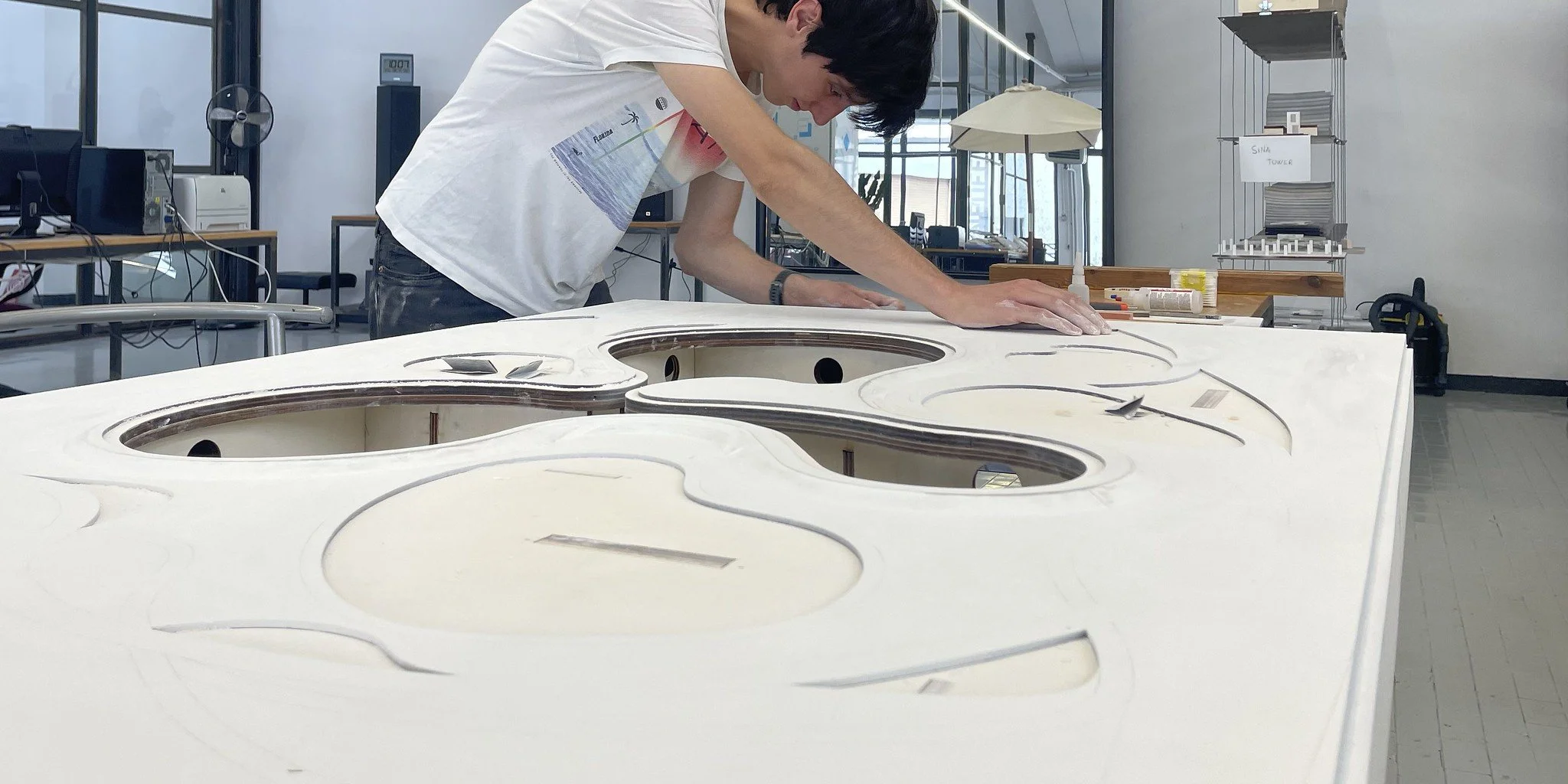 Un model maker ONEOFF Milano sta lavorando su una grande piattaforma di legno con tagli e incavi, nel laboratorio ONEOFF, mentre si concentra e utilizza strumenti e materiali di model making
