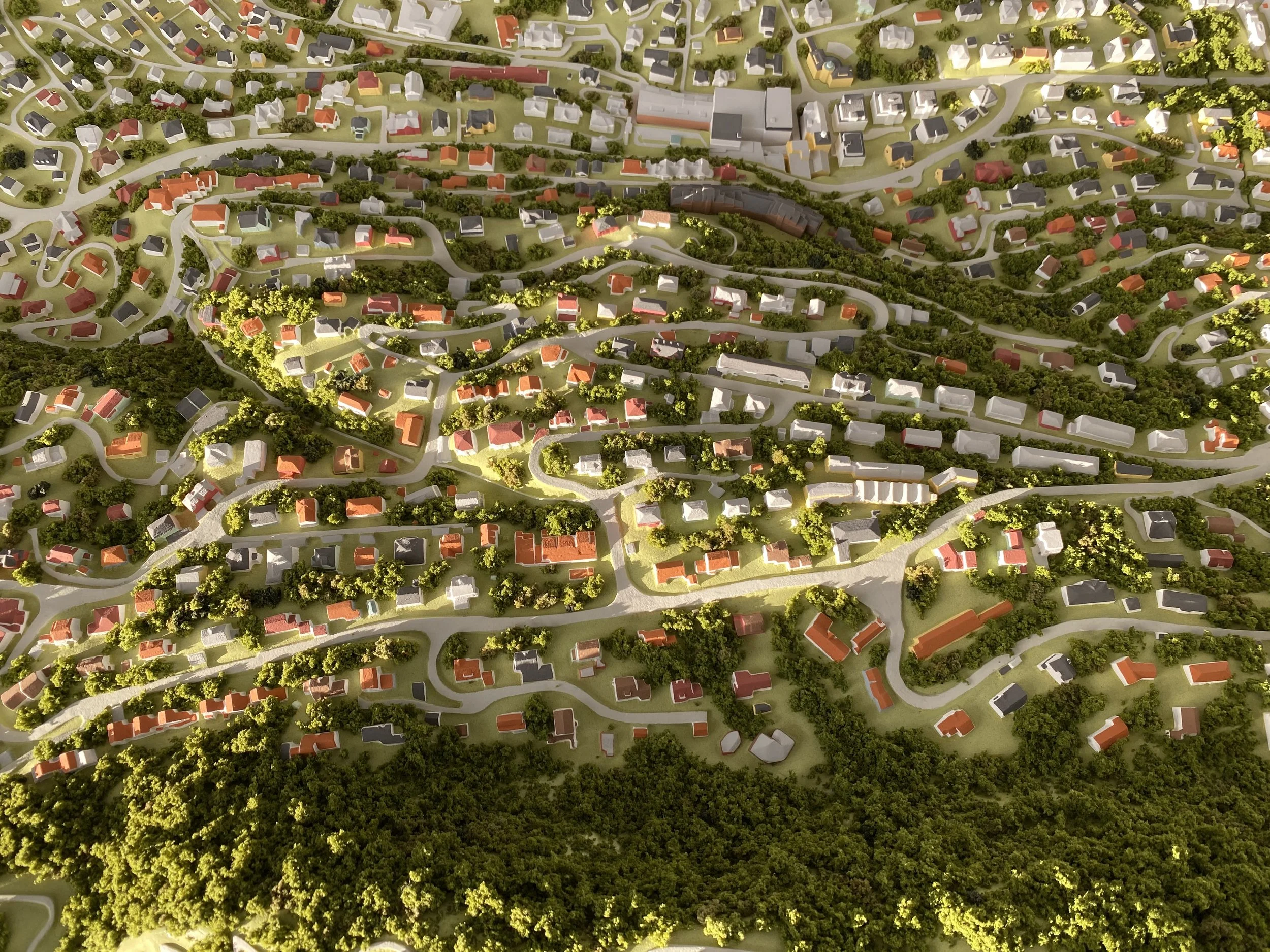 Una veduta aerea di un quartiere residenziale con case di varie dimensioni e colori, circondato da molte aree verdi con alberi e strade curvilinee.