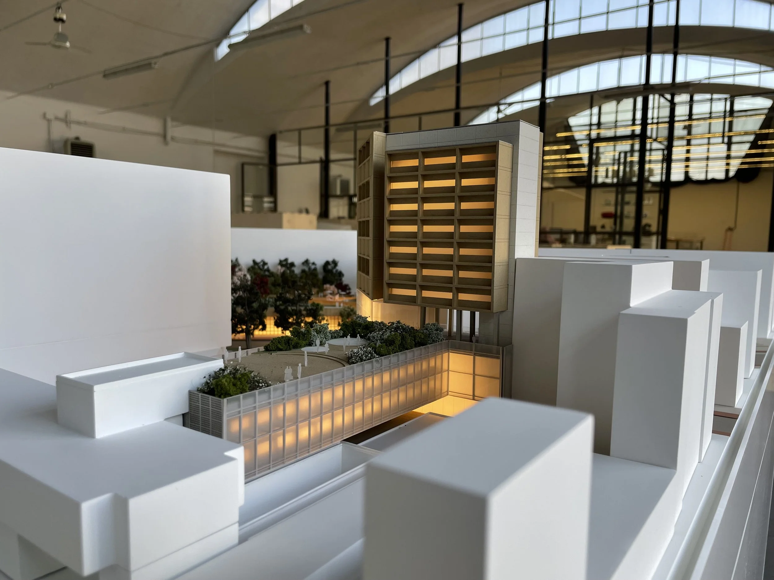 Modello di un edificio in scala con illuminazione calda, con piante e aree verdi, situato in un ambiente interno con grandi finestre e struttura moderna.