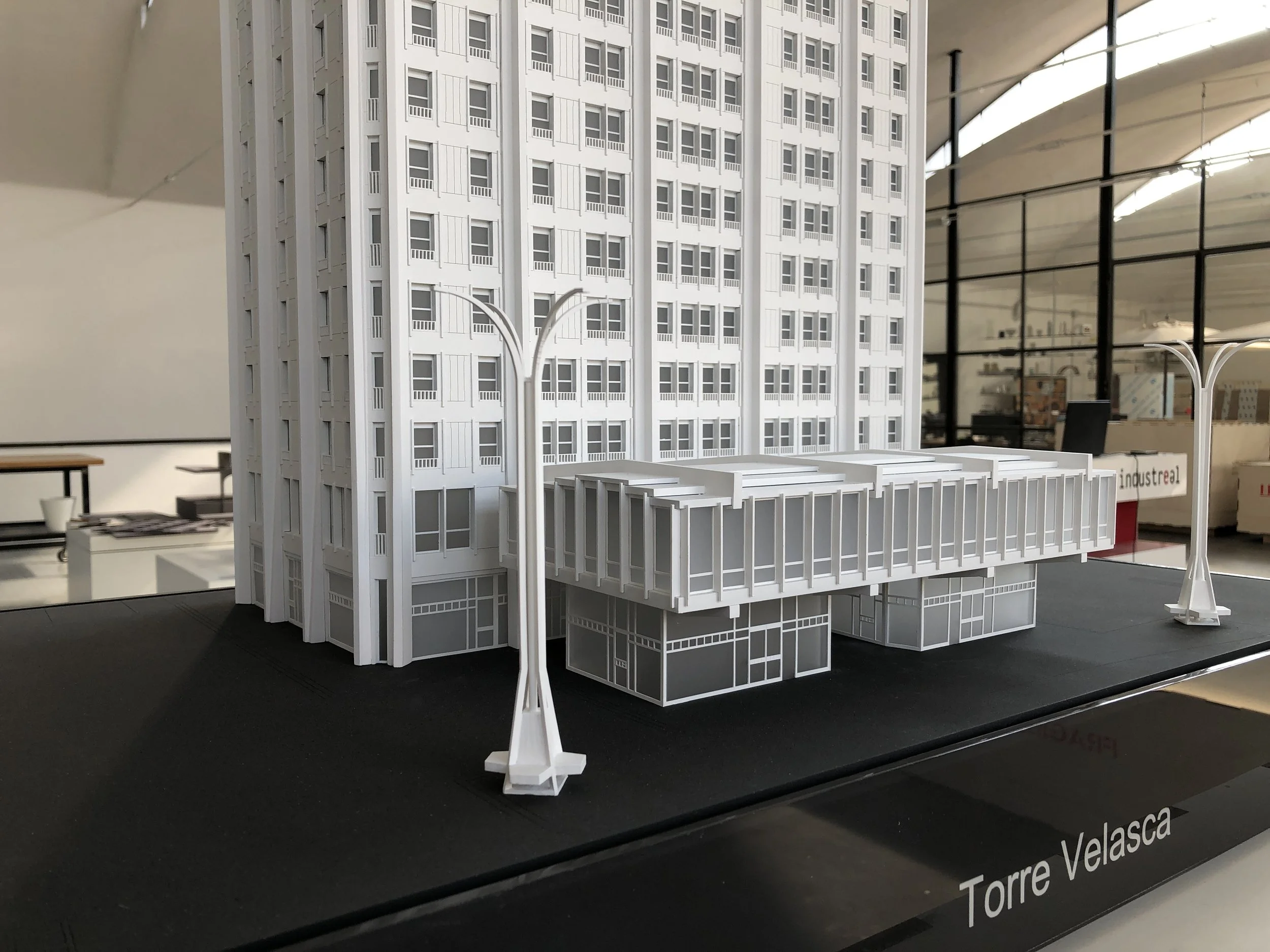 Modello in scala di un edificio alto, bianco, con molte finestre, esposto in una mostra di architettura.