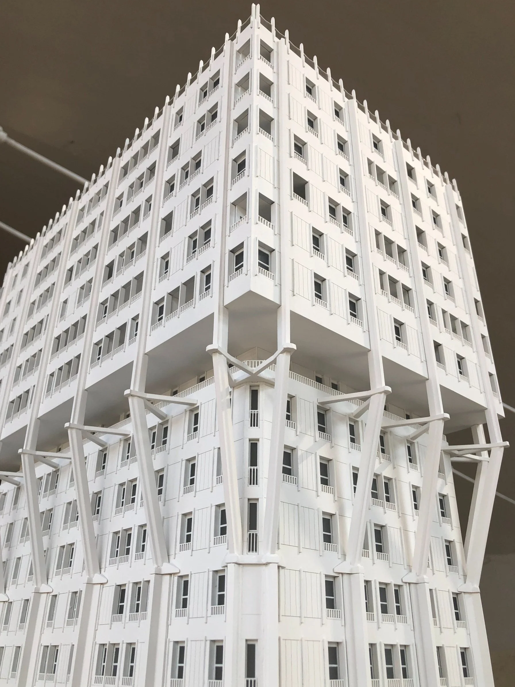 Edificio bianco con molte finestre e balconi, supportato da strutture di supporto a forma di X.