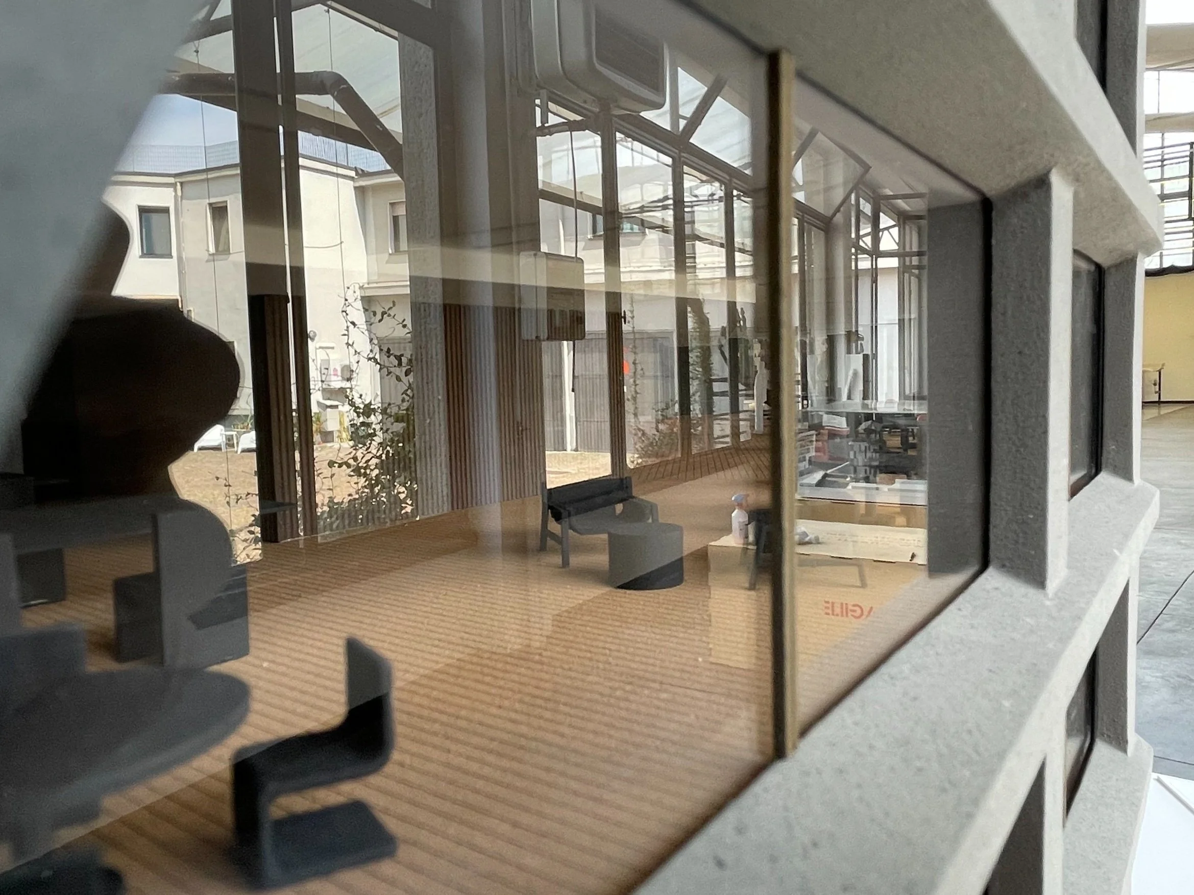 Reflections di edifici e strutture di vetro e cemento visibili attraverso una finestra con grate di ferro, all'interno di un ambiente con pavimento di parquet e pareti di cemento.