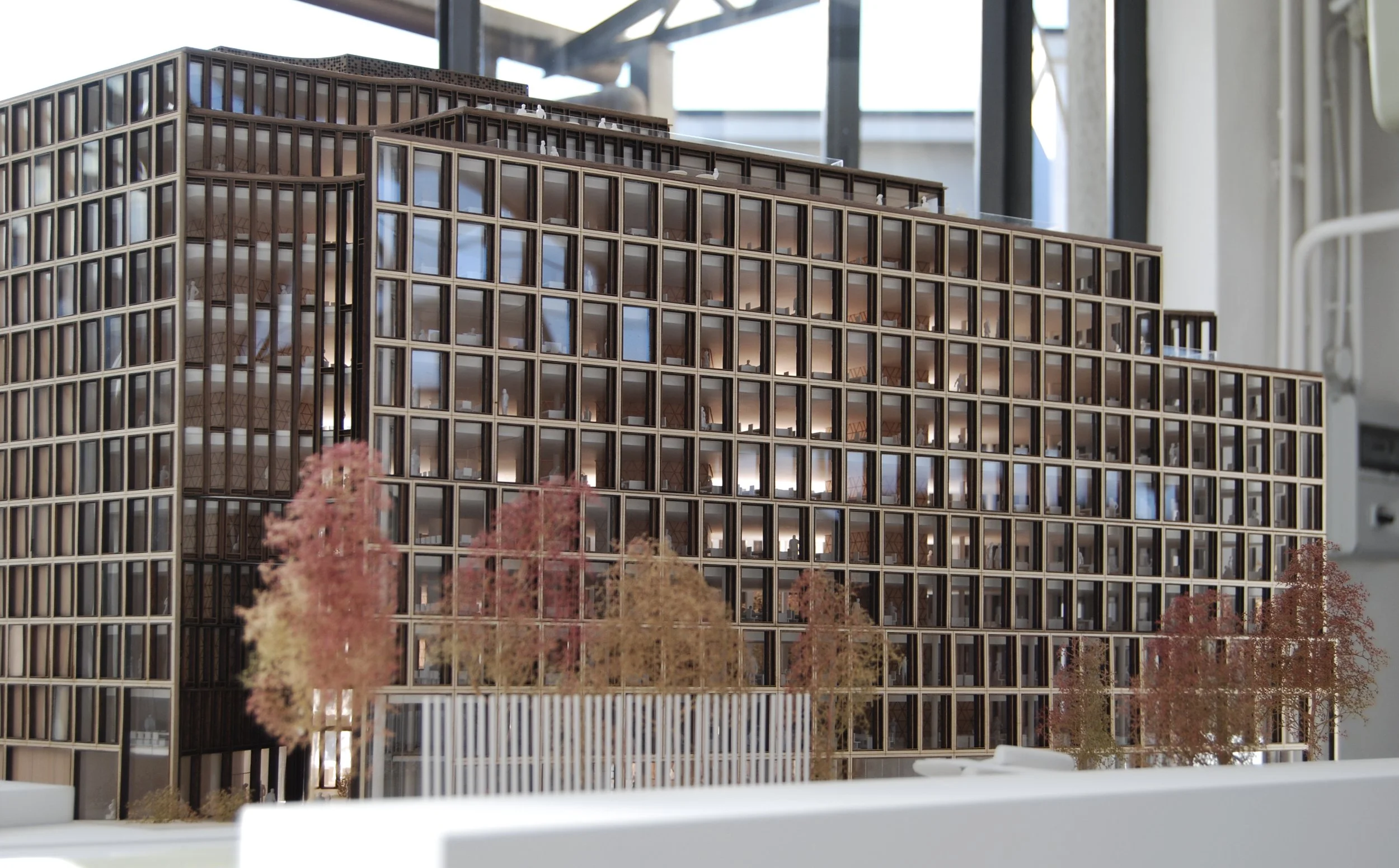 Modello di un edificio in miniatura con strutture esterne in legno e interni illuminati, circondato da alberi con foglie autunnali.