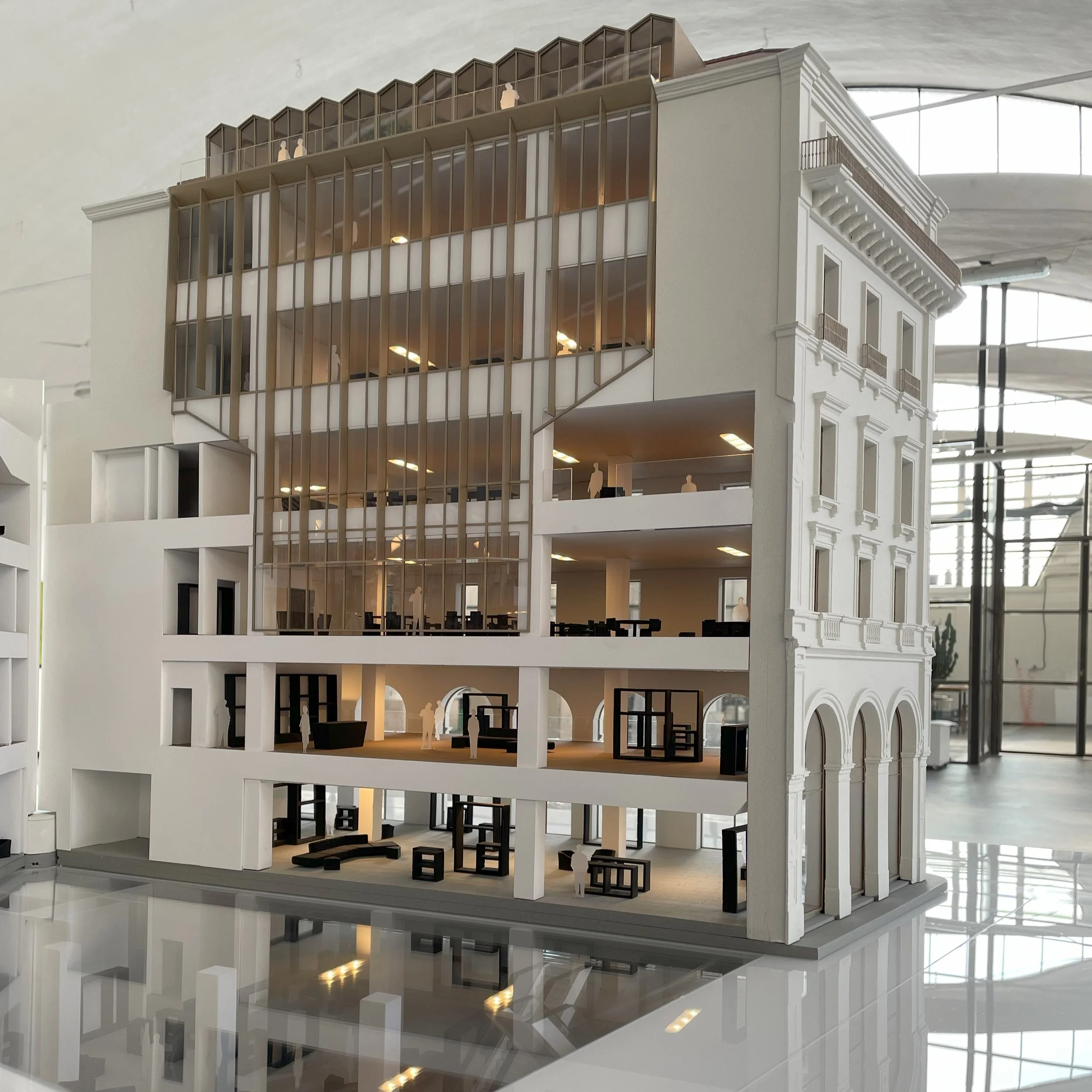 Modello architettonico di un edificio con facciata mista tra stile moderno e classico, con balconi e grandi finestre, visibile all'interno di un edificio con grande vetrata sopra