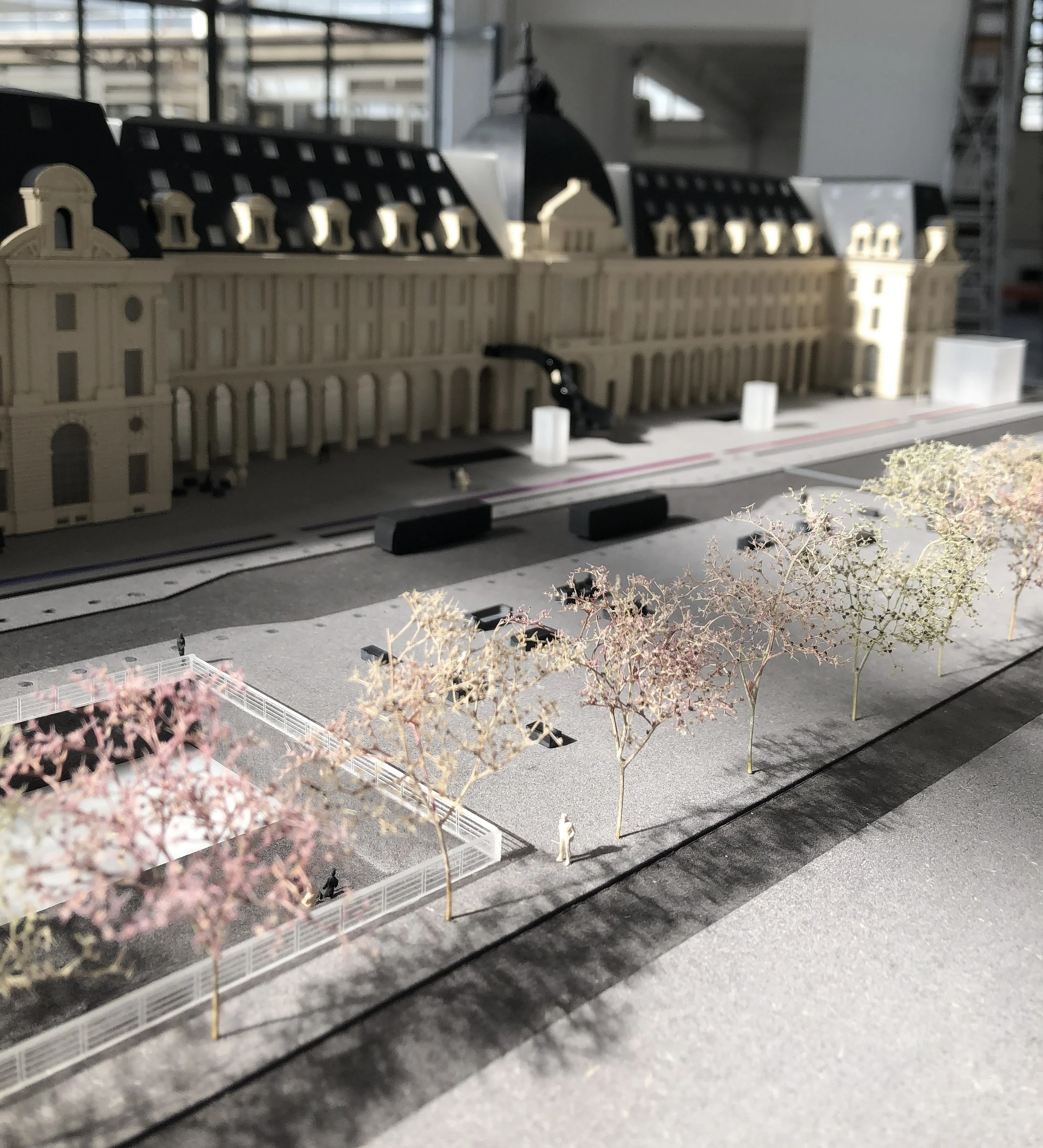 Modello in scala di un edificio storico con dettagli architettonici, piante finte e la struttura in plastica è visibile su un tavolo, con una finestra e un edificio moderno sullo sfondo.