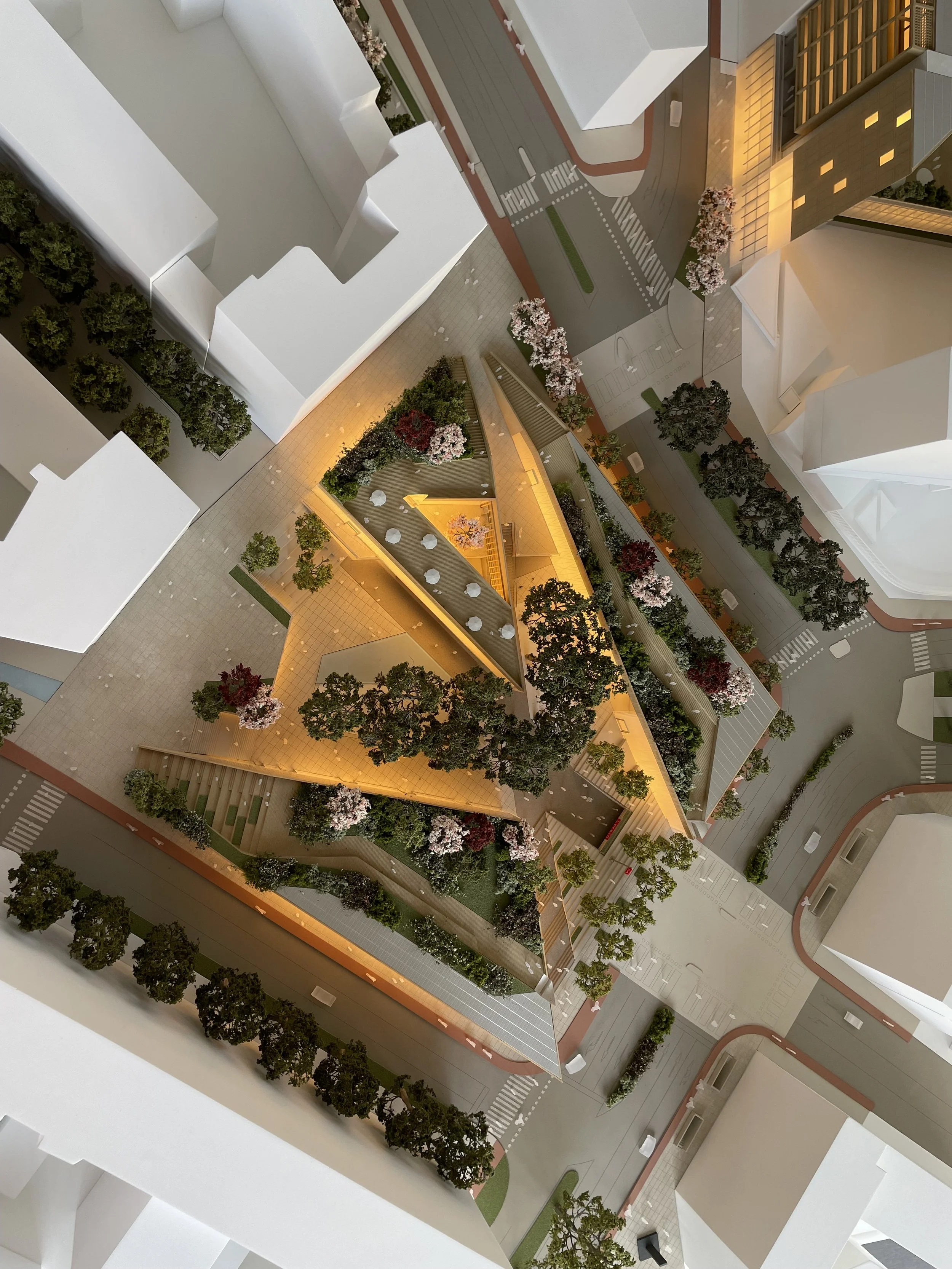Un modello architettonico di un complesso residenziale con cortili, alberi e aree verdi, illuminato da luci calde di sera.