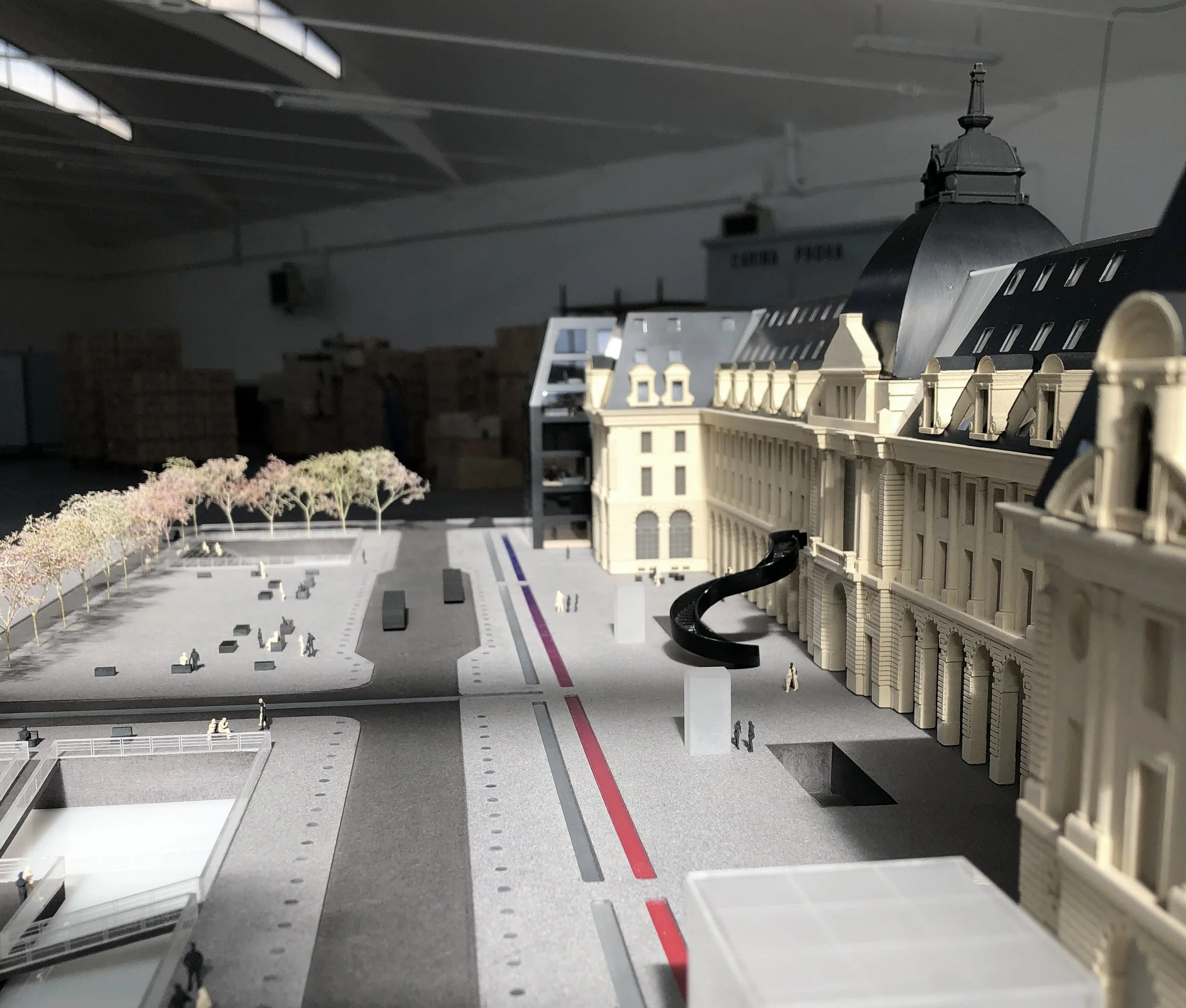 Modellino di un edificio storico con molte finestre e tetto a pendenza, altri edifici e alberi in scala nel contesto di una mostra o di un progetto di architettura.