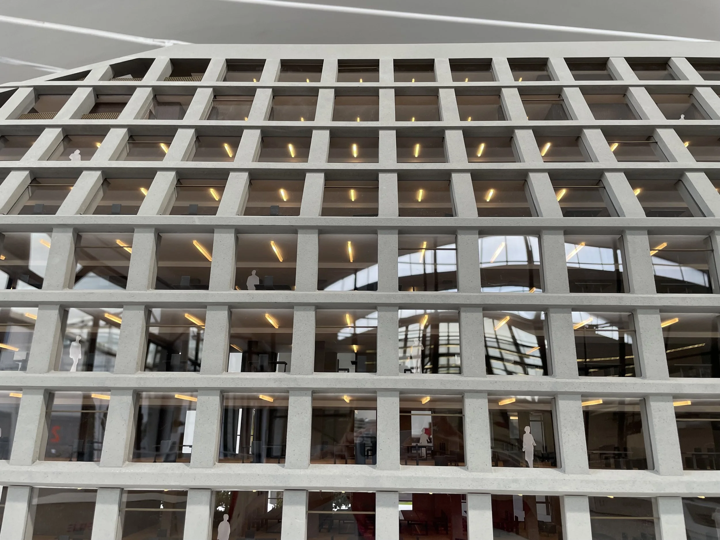 Immagine di un edificio moderno con strutture di cemento e finestre quadrate in più livelli, visibili anche alcune persone all'interno delle finestre, illuminazione interna visibile.