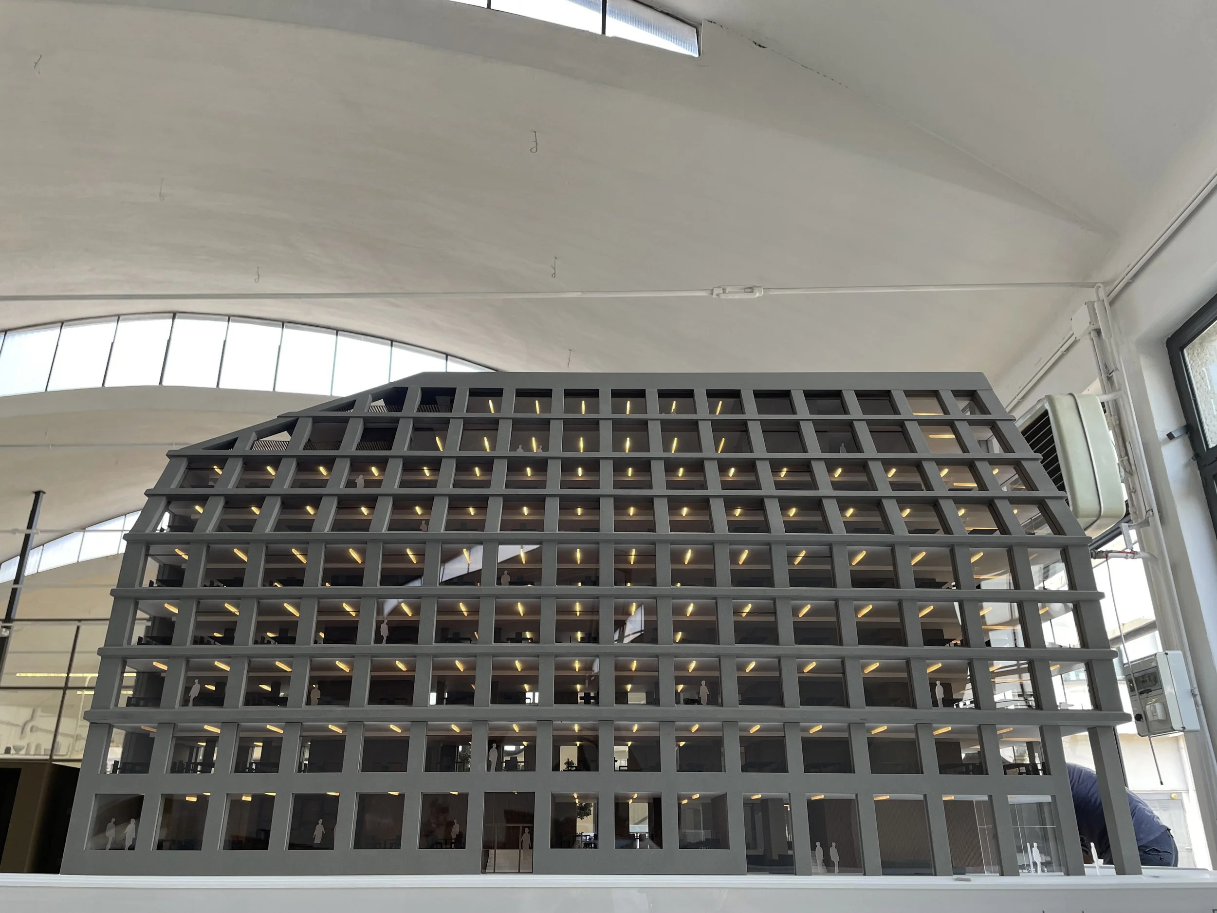Interno di un edificio moderno con grandi finestre e una struttura a più piani visibile.