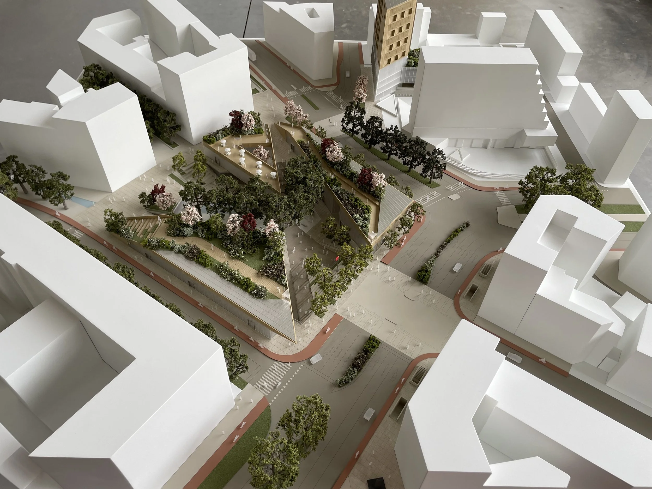 Modello architettonico di un'area urbana con edifici bianchi, strade, marciapiedi, alberi e spazi verdi, inclusa una zona con tavoli e sedie.