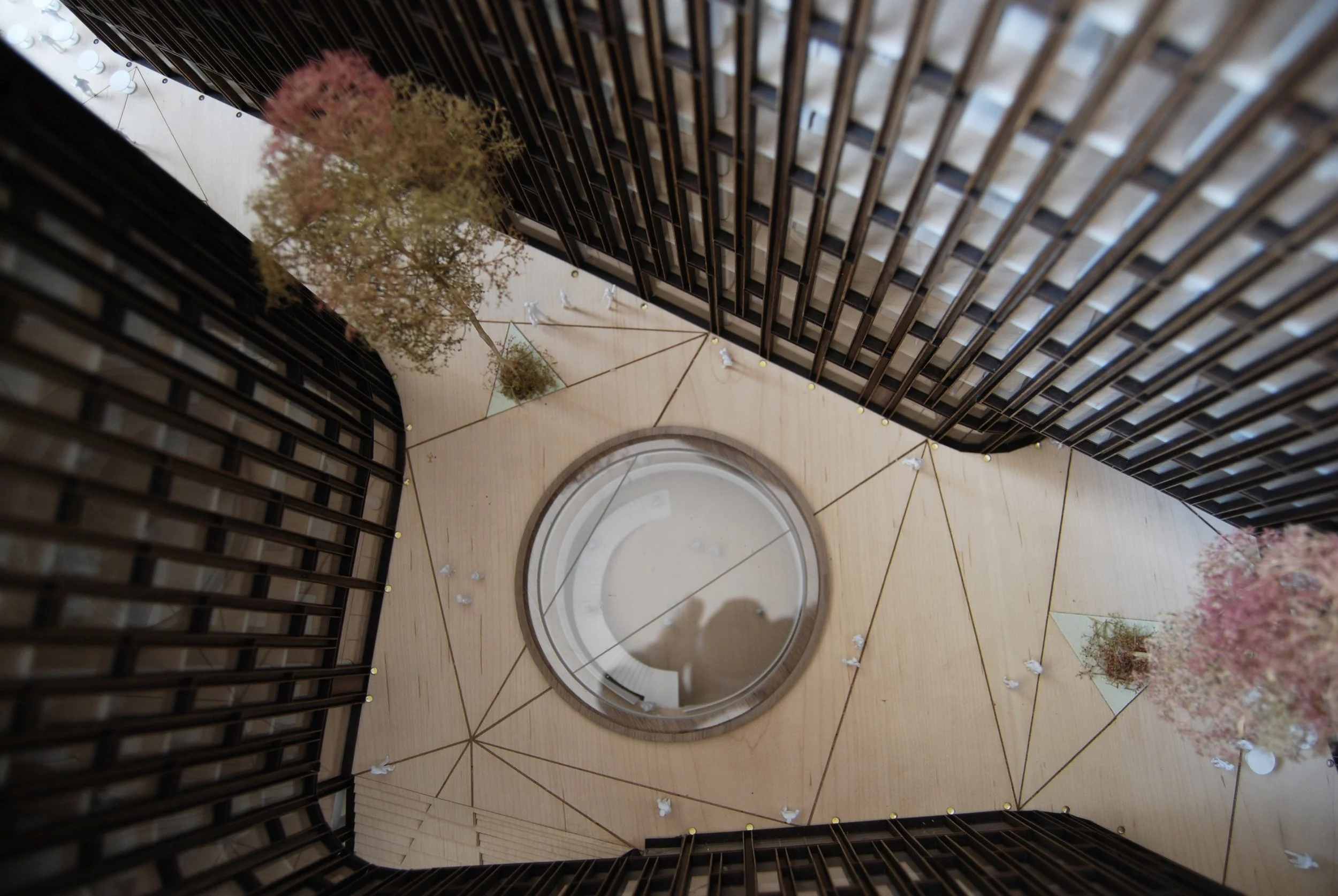 Interno di un edificio con pareti in stile moderno, decorato con fiori artificiali e luci, con una grande apertura circolare sul pavimento e strutture di legno in leggera curvatura.