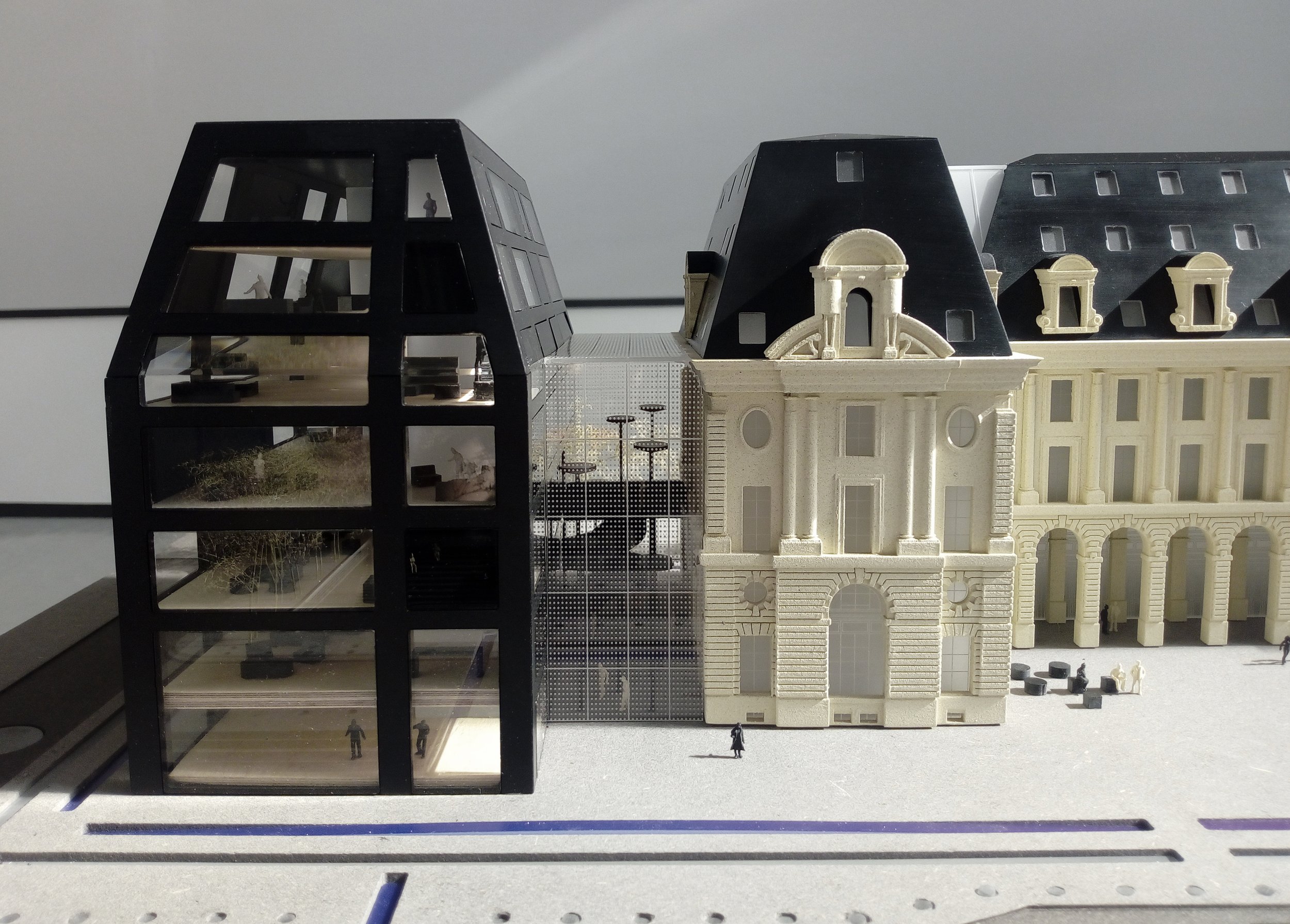 Modello in scala di un complesso edilizio con edifici storici e moderni, inclusa una struttura in vetro e acciaio con figure minime, rappresentando un mix di architettura classica e contemporanea.