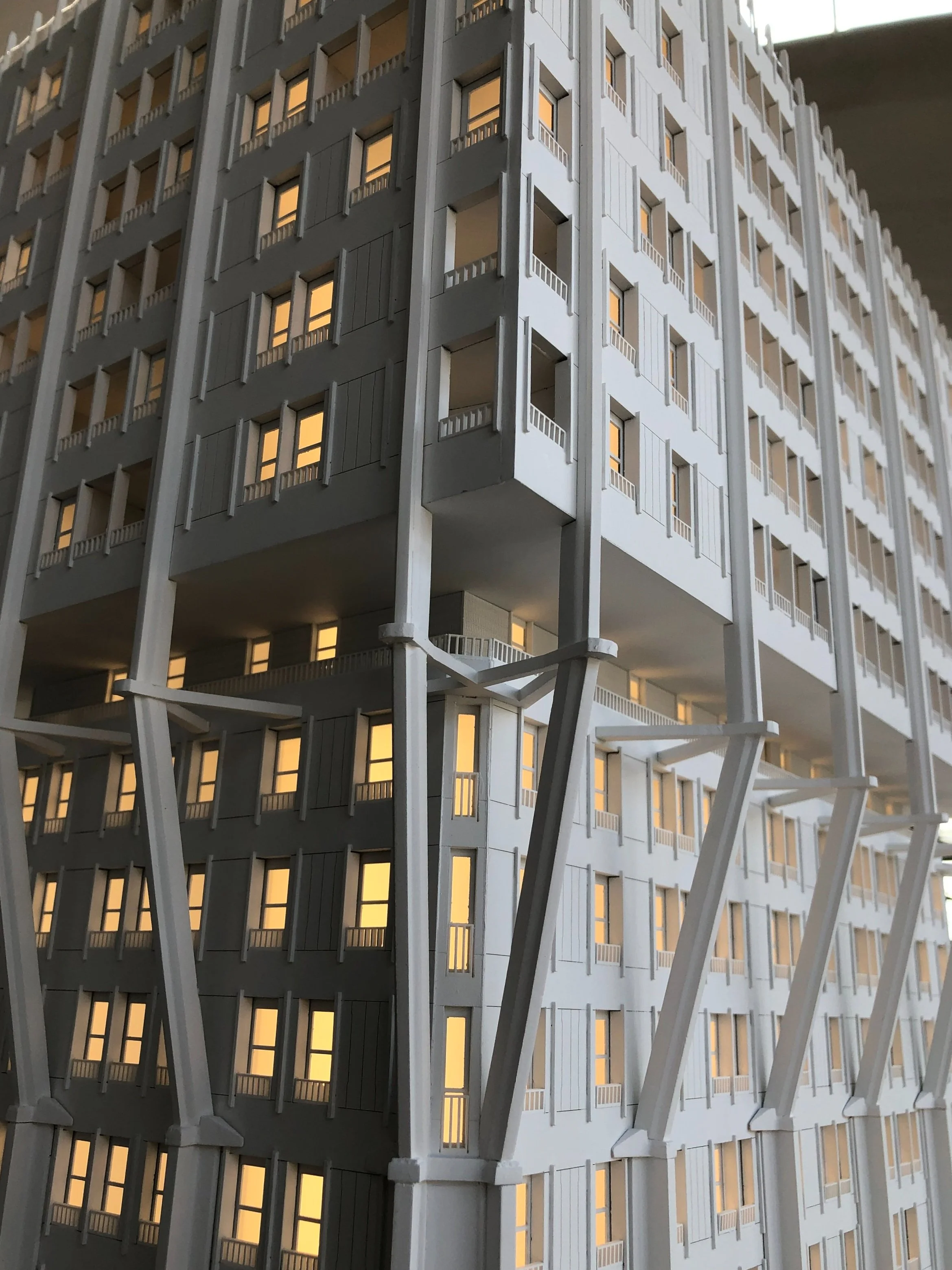 Vista di un edificio moderno con molte finestre illuminate, con un design architettonico originale e strutture di supporto visibili in primo piano.
