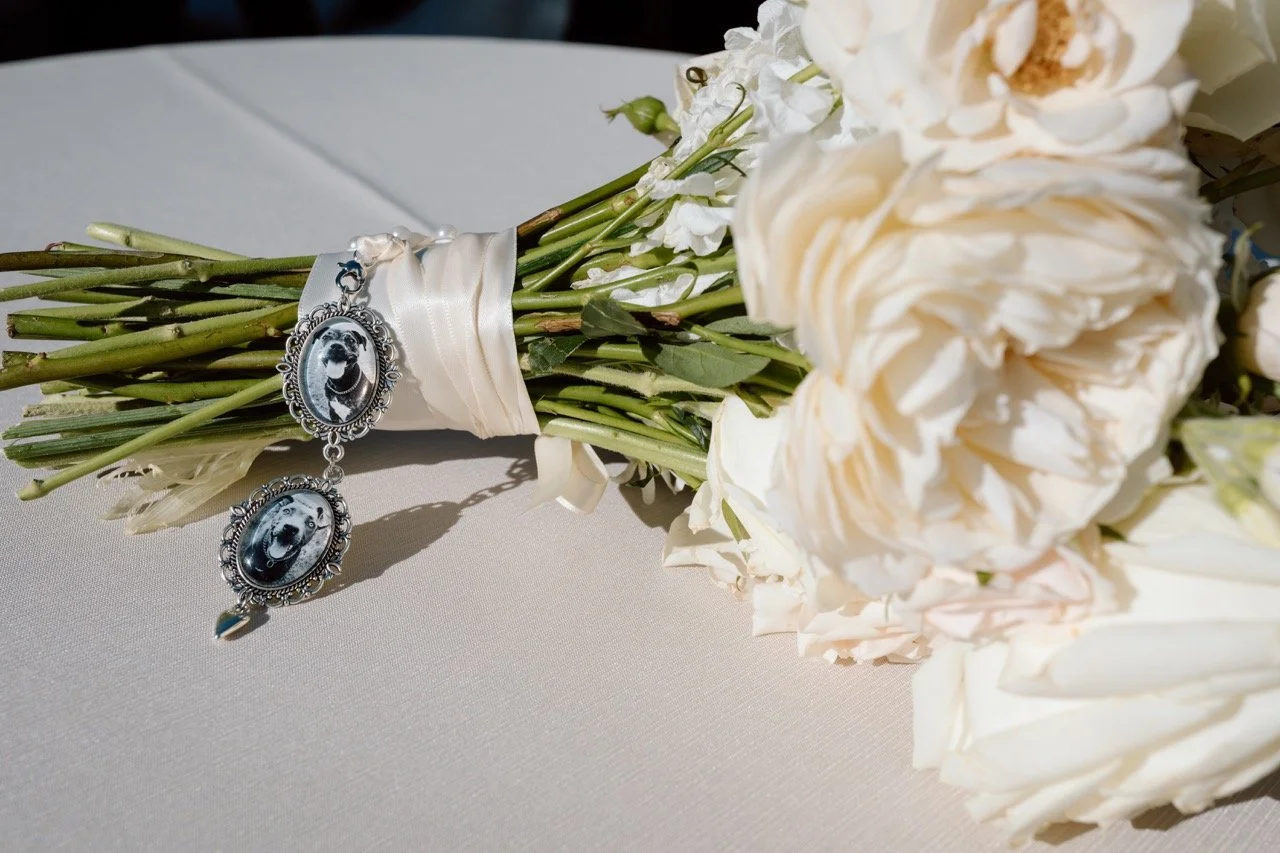 A bouquet of white roses attached with a white ribbon, with a silver photo charm featuring a picture of a dog.
