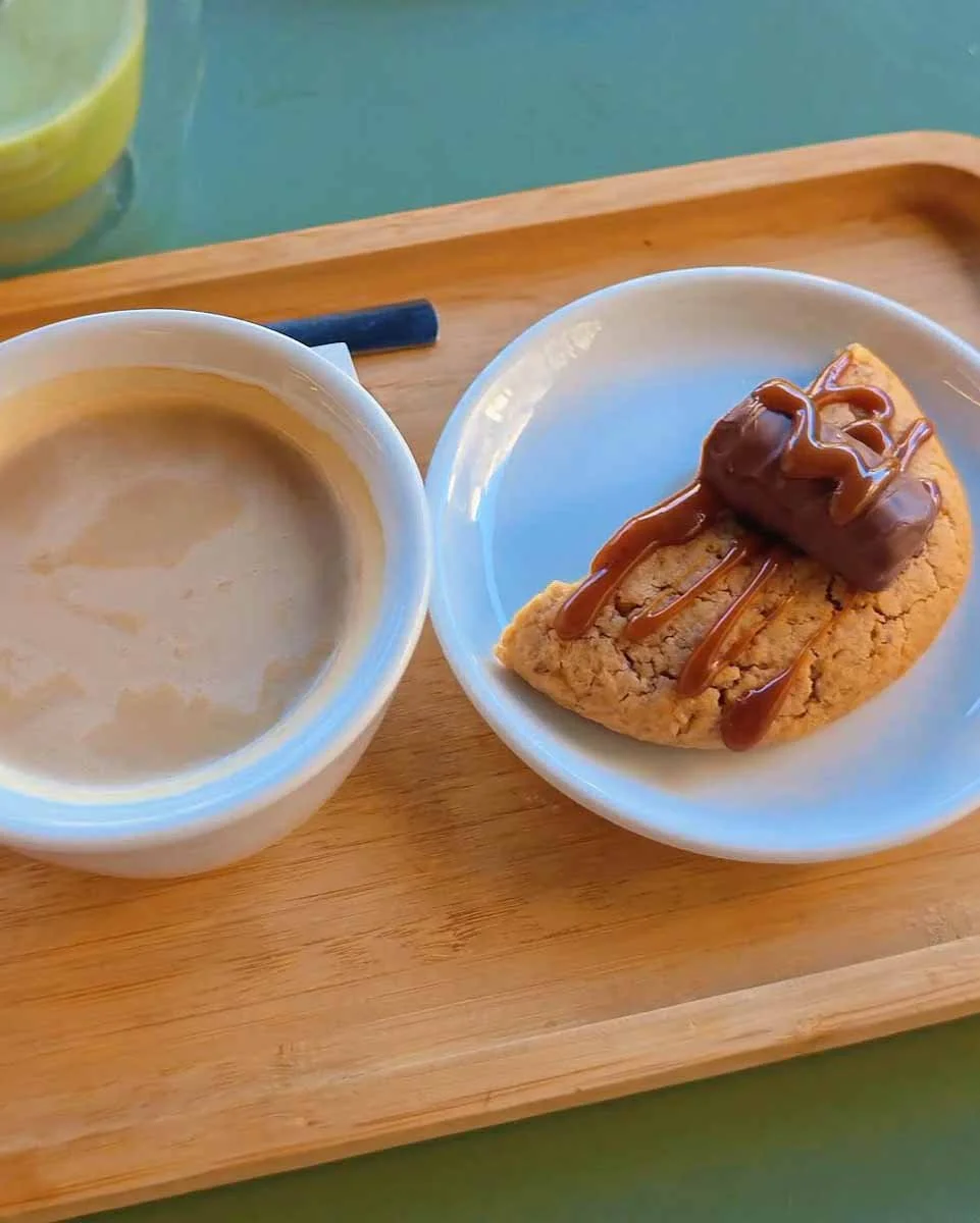 Tasse de café au lait accompagnée d'un demi cookie saveur twix, sur un mini plateau en bois