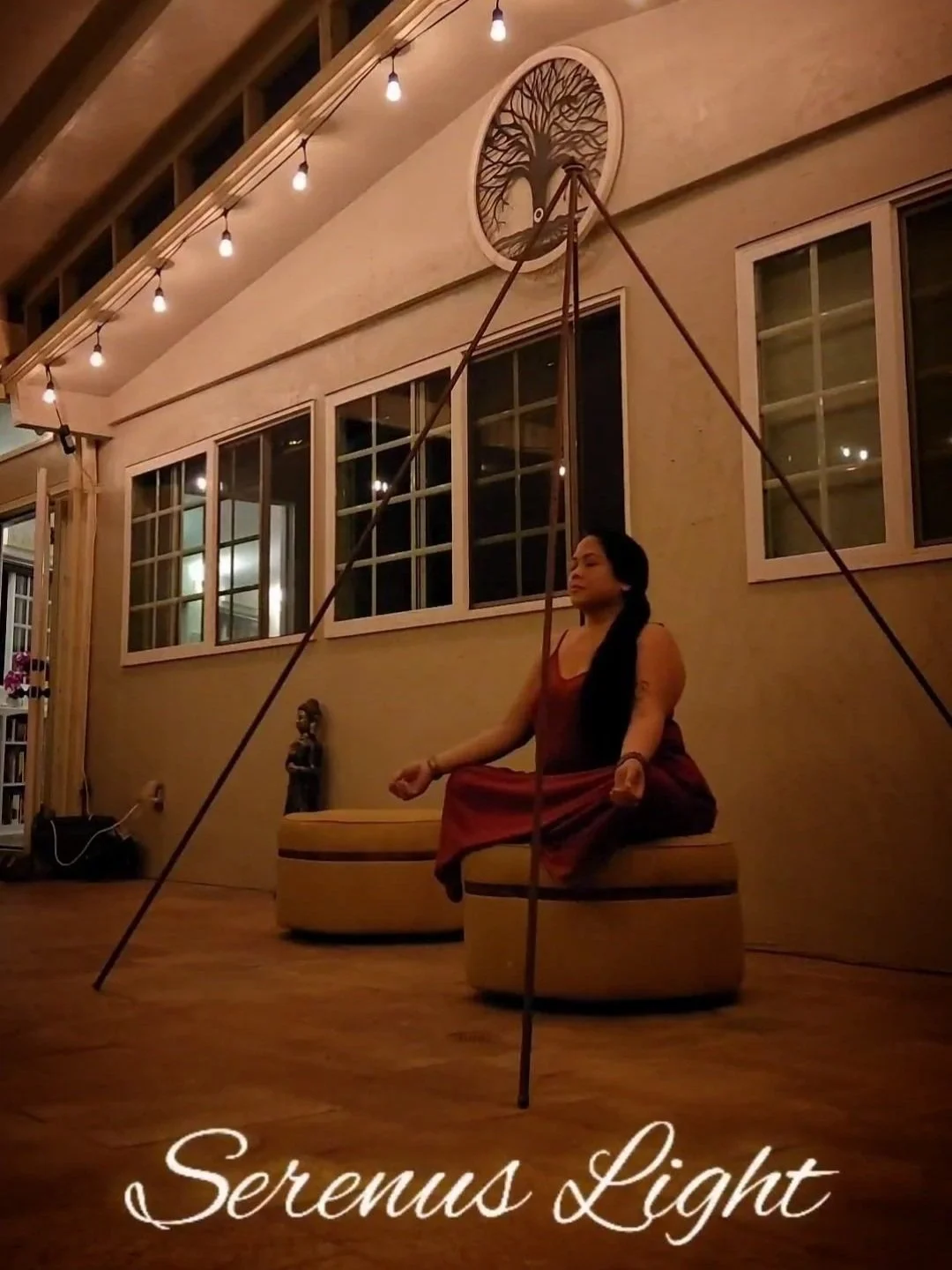 A woman practicing meditation in a dimly lit outdoor space at night, sitting cross-legged on a bench with a serene expression, surrounded by warm lighting and decorative elements.