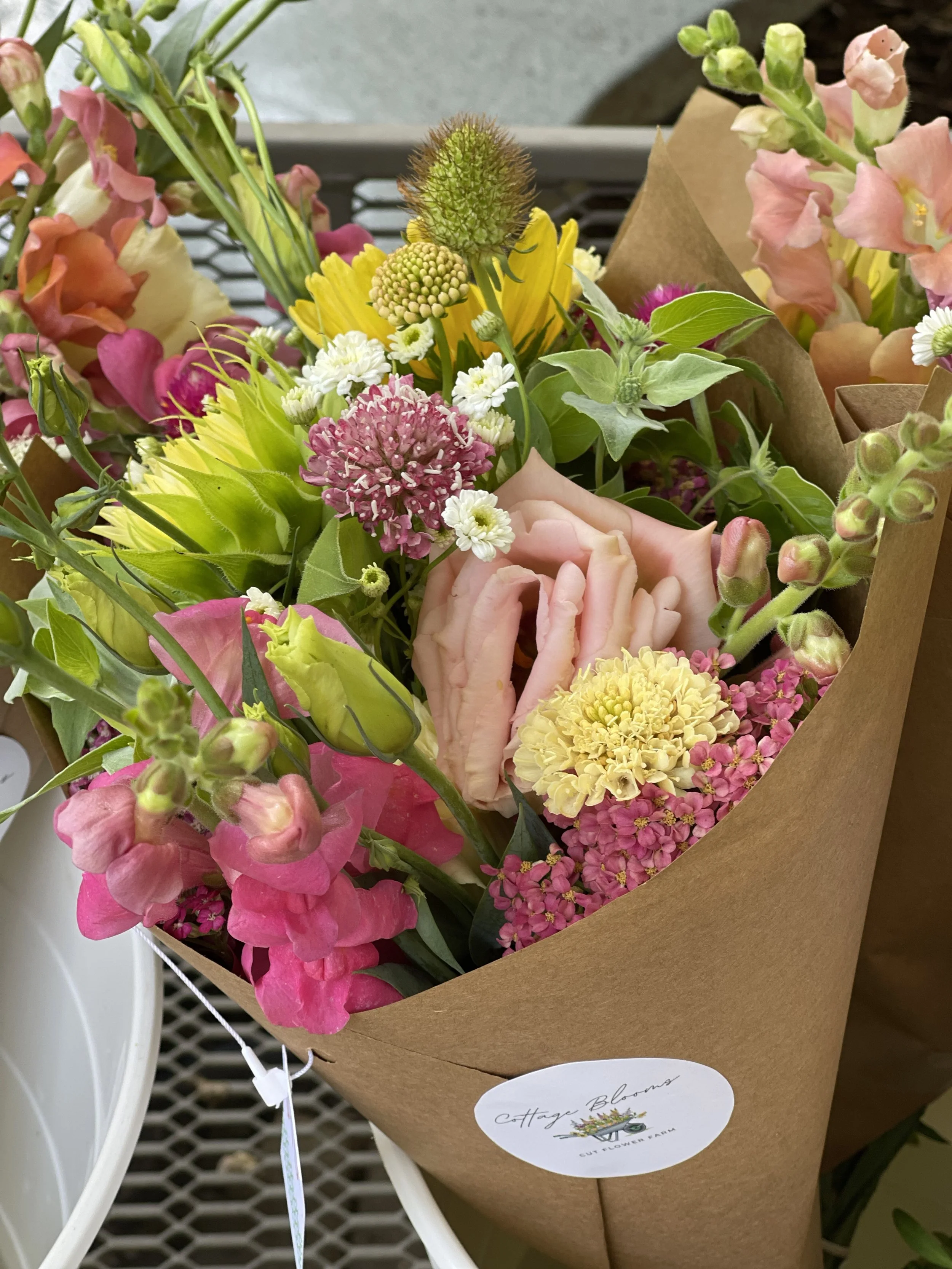 A bouquet of assorted colorful flowers in brown wrapping paper, labeled 'Cottage Blooms'.