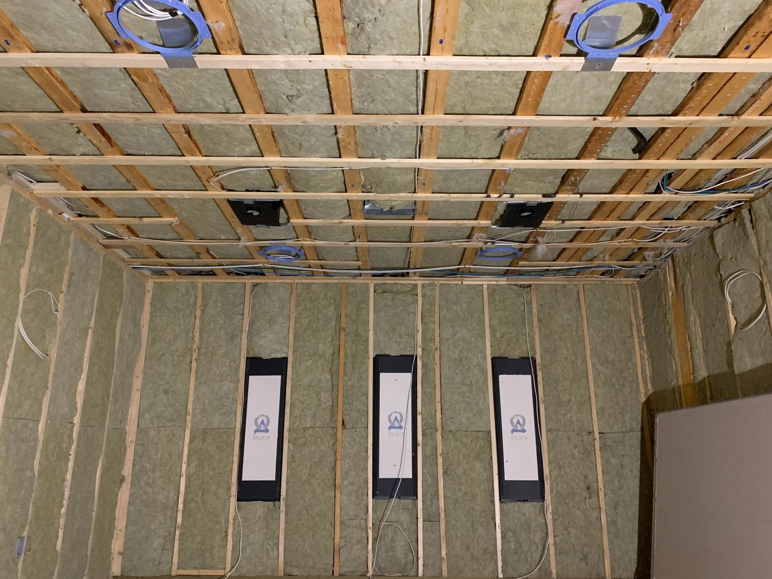 Construction of an ATMOS theater room with exposed wooden framing, insulation, and mounted electrical devices on the wall.