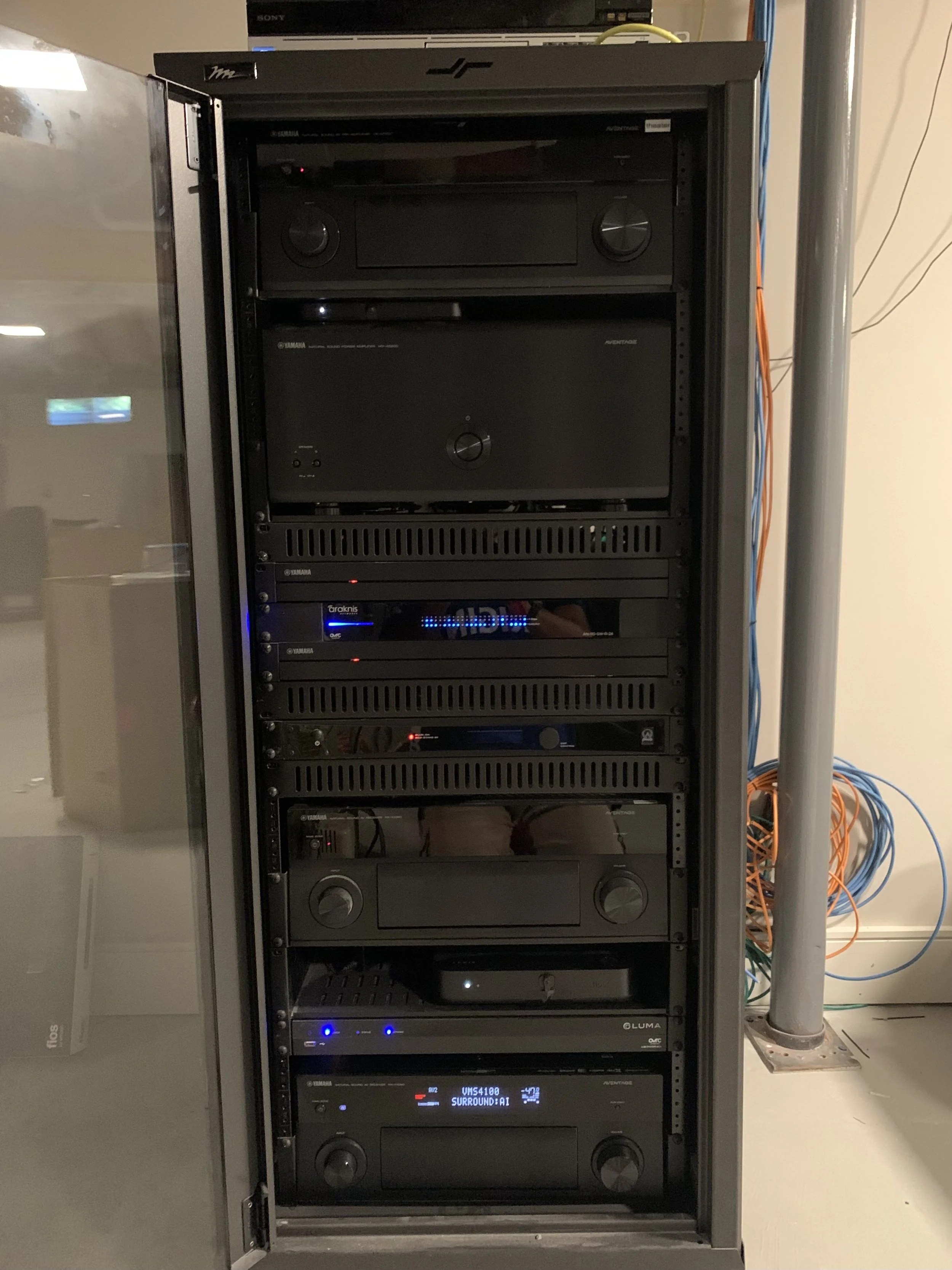 A tall black server rack containing multiple electronic devices, including audio and video equipment, with cables on the side.