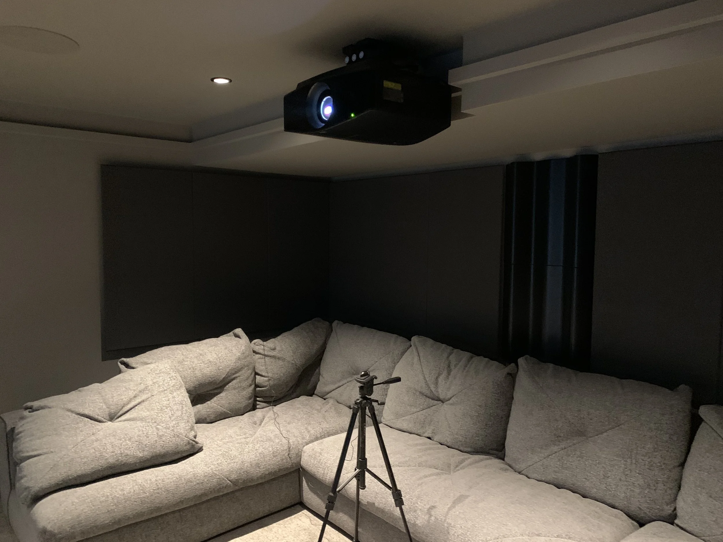A gray L-shaped sectional sofa with several cushions in a room with dark walls and a Sony laser  projector.