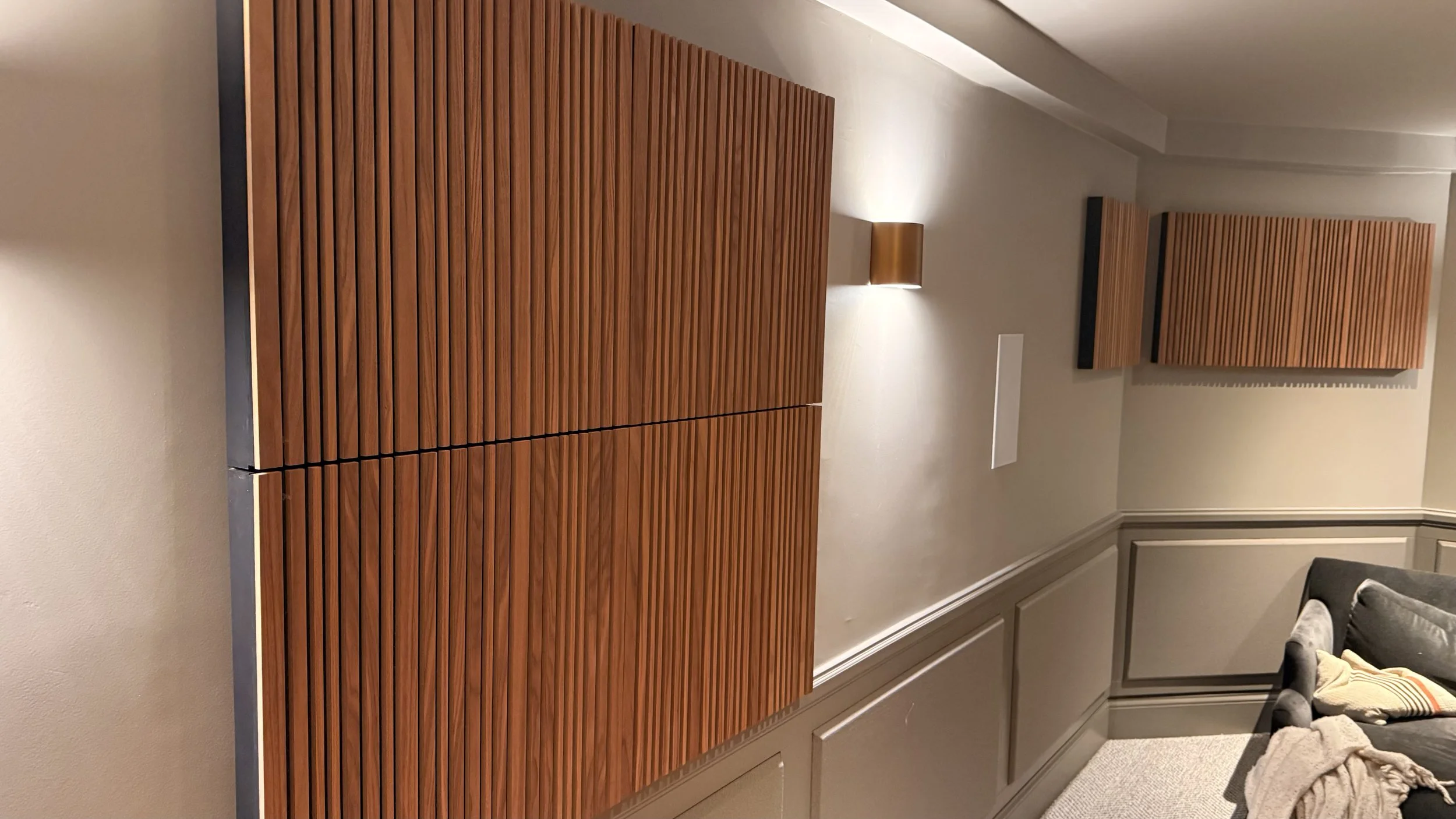 Interior of a room with wooden acoustic panels on the walls, a cushioned sofa with pillows, and wall-mounted lights.