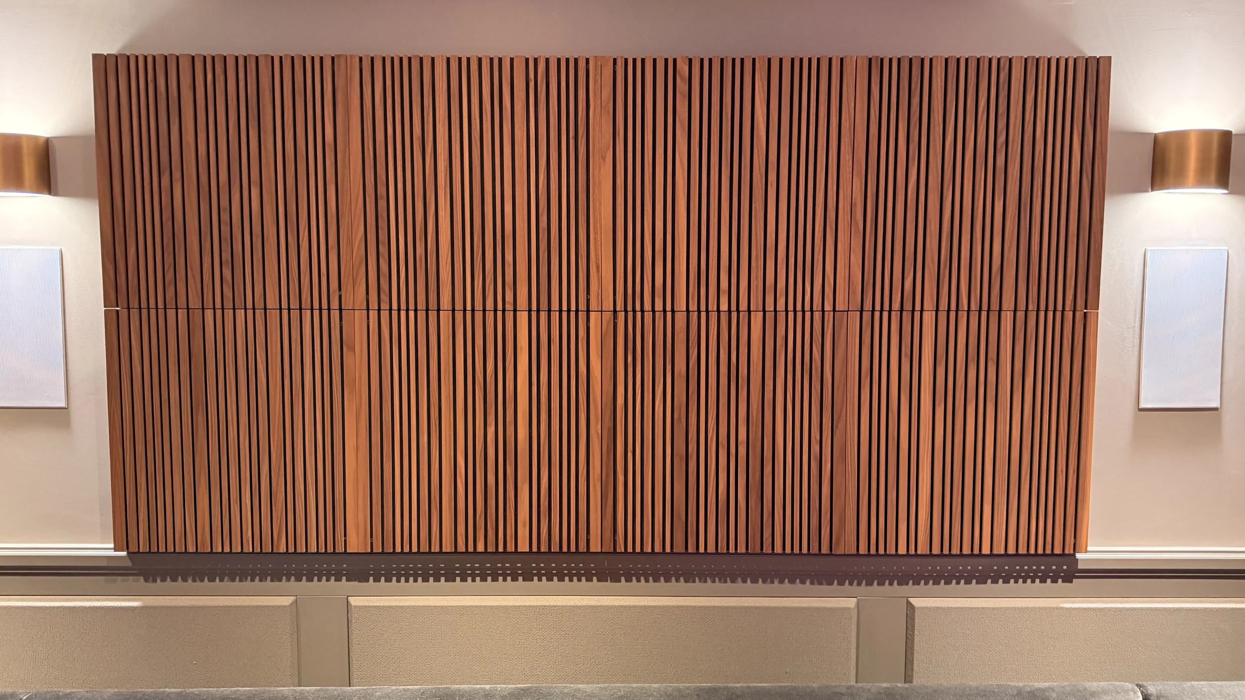 Interior wall with wooden acoustic panels, two wall-mounted white speakers, and two wall lamps on either side in a modern setting.
