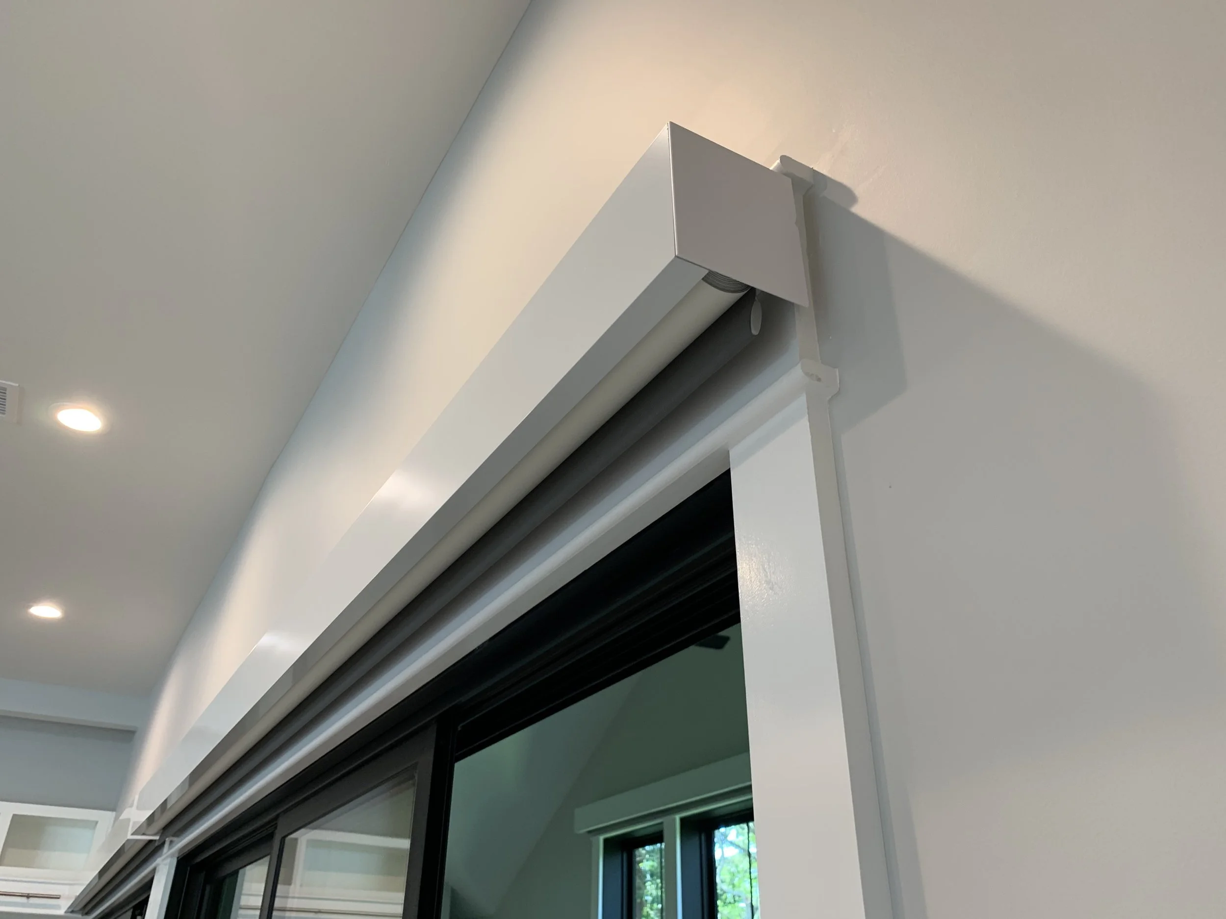 Close-up of a white window air conditioning unit installed near the ceiling, with the wall and ceiling visible, Lutron Triathalon shades.