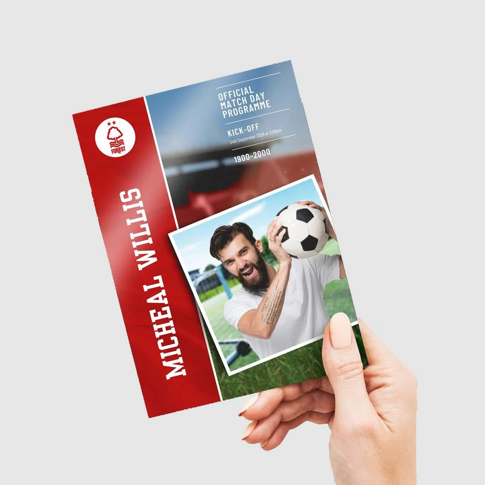 A hand holding a football themed funeral order of service booklet program featuring a man with a beard holding a soccer ball, with a stadium in the background.