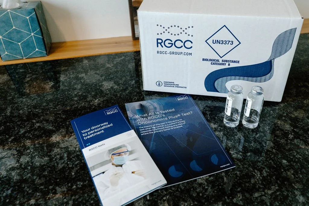 A box labeled RGCC with vials of clear liquid and informational brochures on a dark speckled countertop.
