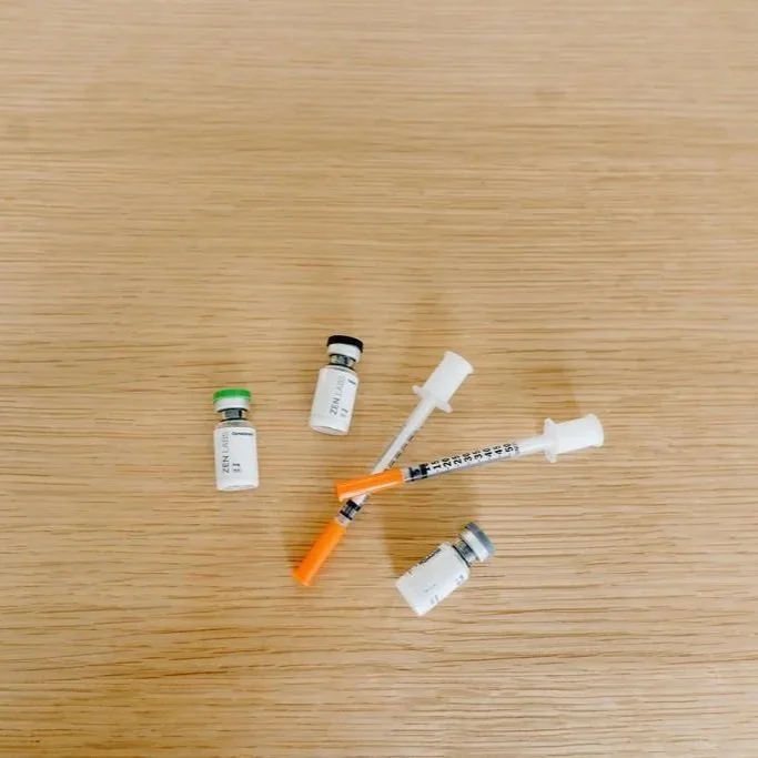 Four vaccination vials and two syringes on a wooden surface.