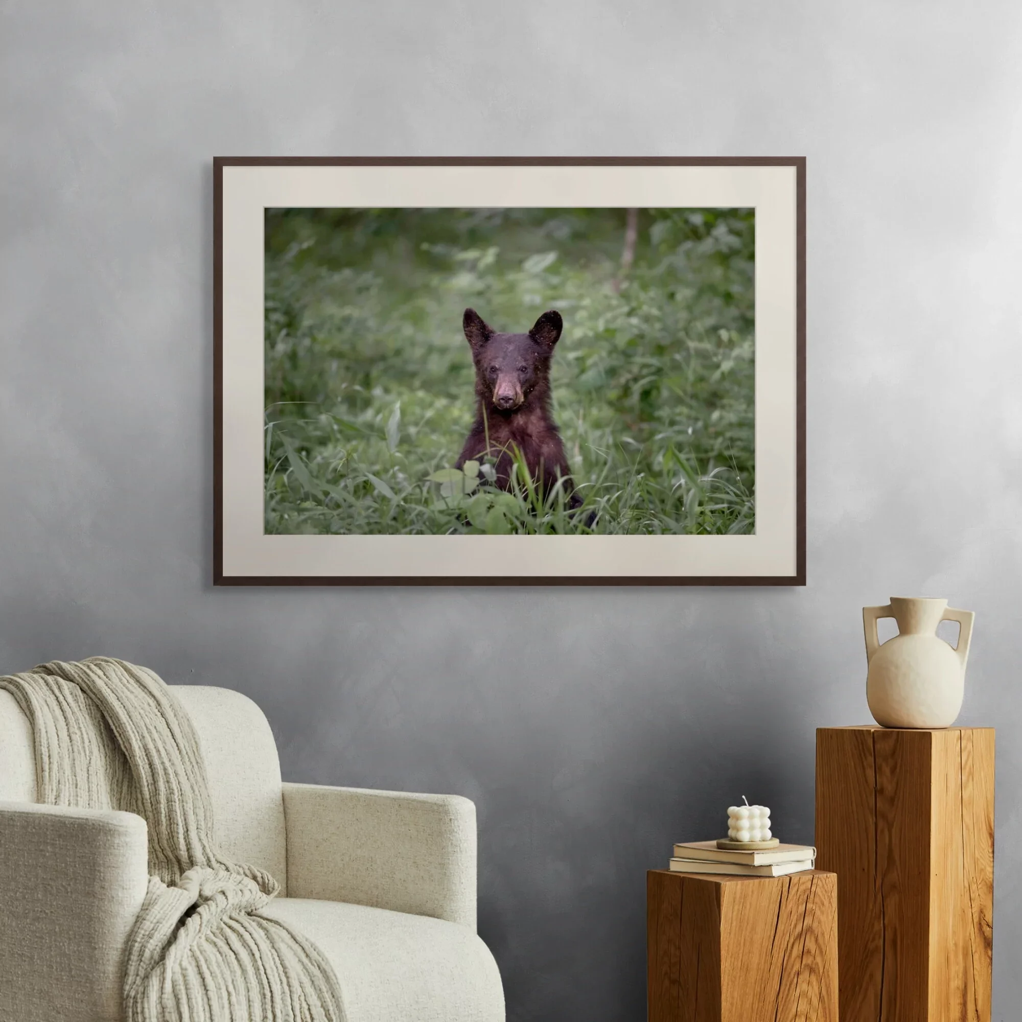 A fine art print of a black bear standing in a field of grass hanging on a wall.