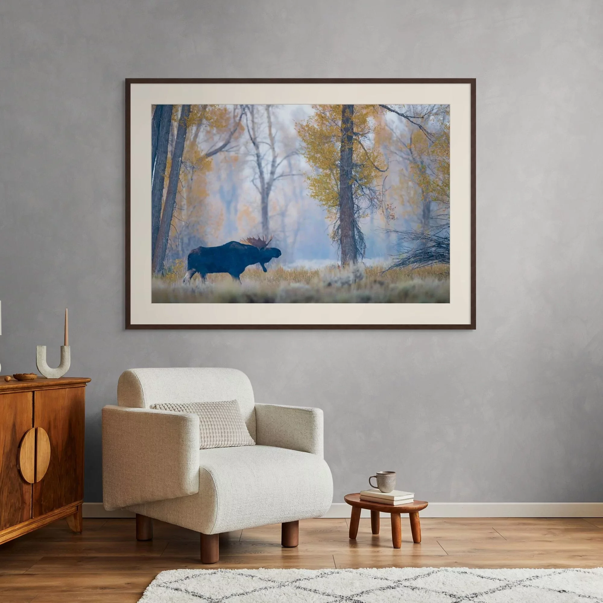 Living room with beige sofa, round wooden side table, and a framed landscape painting of trees and a moose on the wall.