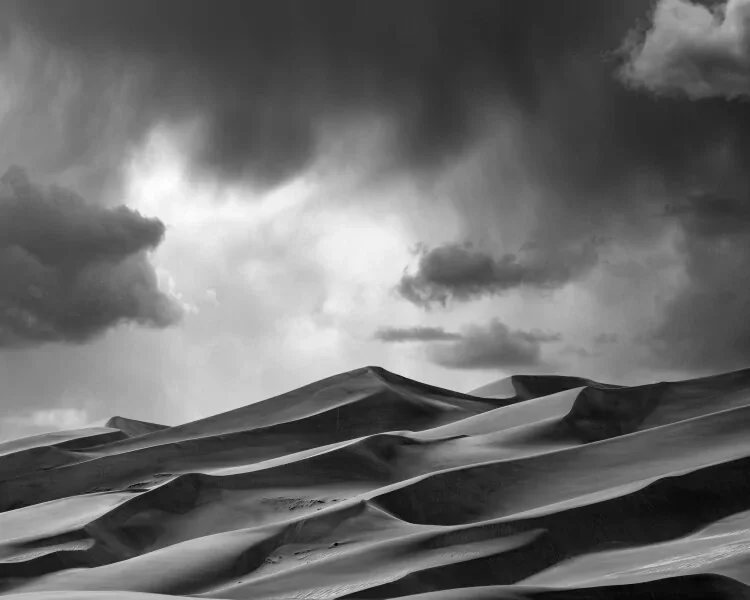 Black and white photograph of sand dunes under a cloudy sky.