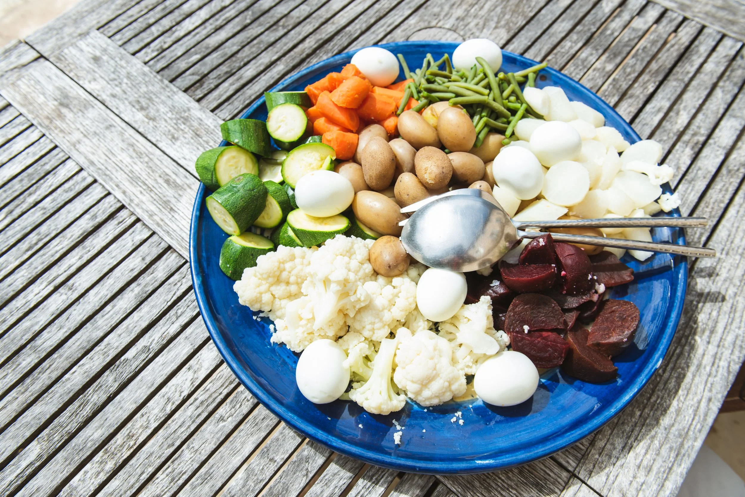 A blue plate filled with assorted raw vegetables and cheeses on a wooden table outdoors. wellness coach portland