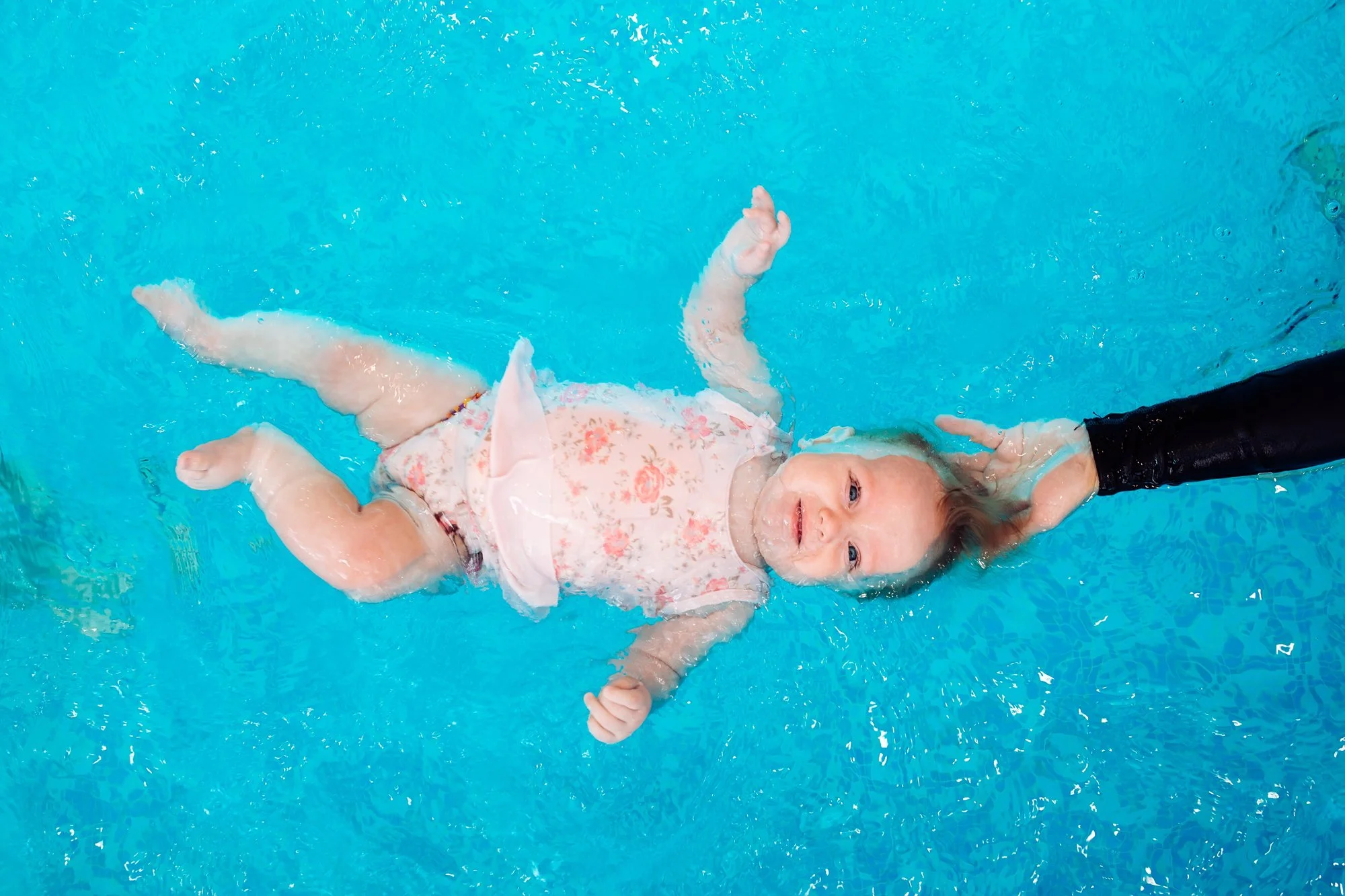  Baby floating on back with the support of and adult holding their head above the water. 