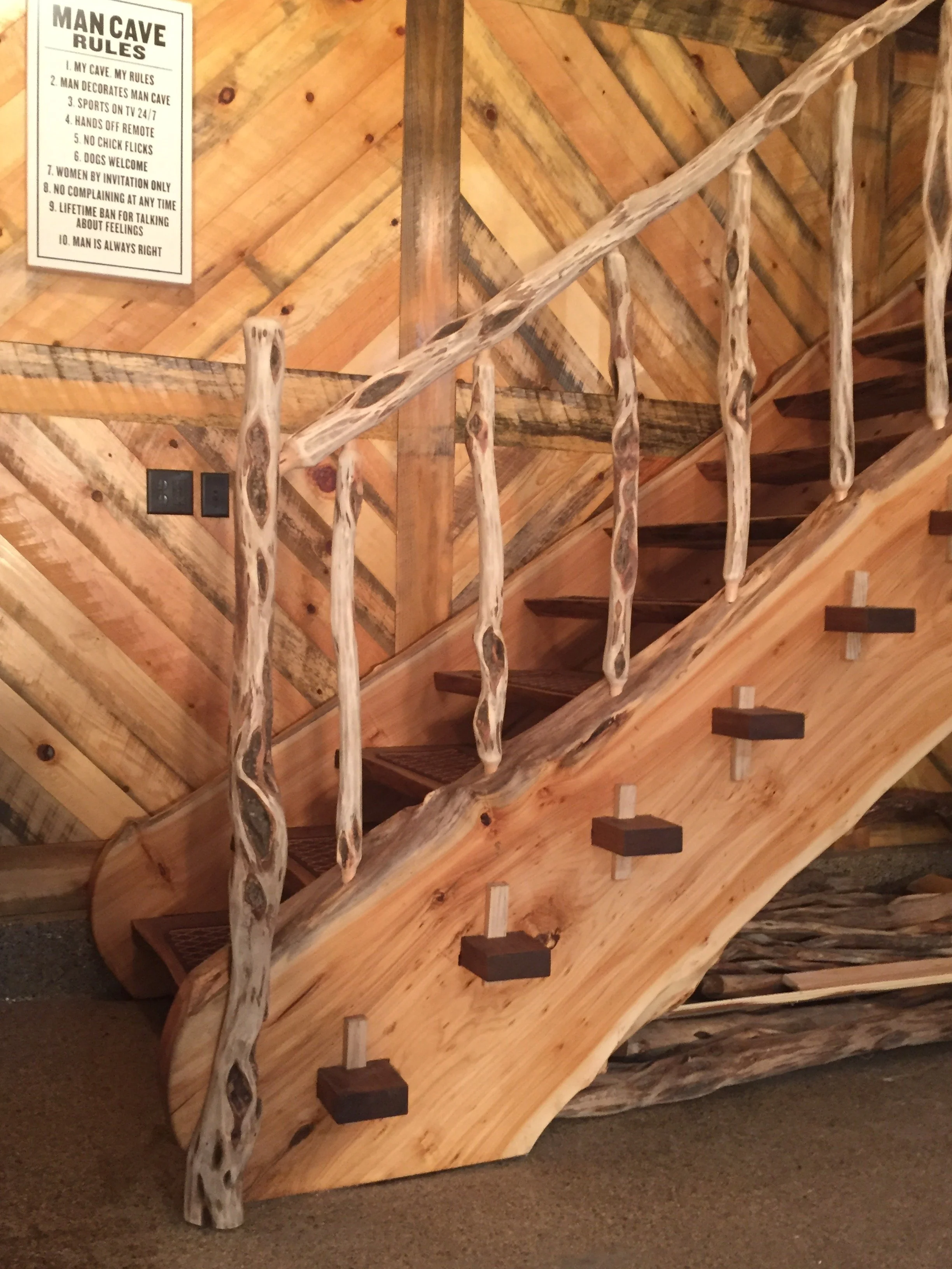 Wooden staircase with carved, rustic handrails and a wall-mounted sign with rules for a man cave.