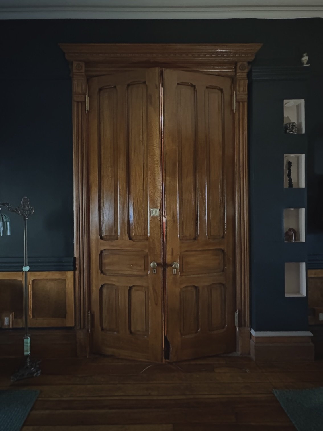 Wooden double doors in a dark room, with decorative trim and built-in shelves on the right.