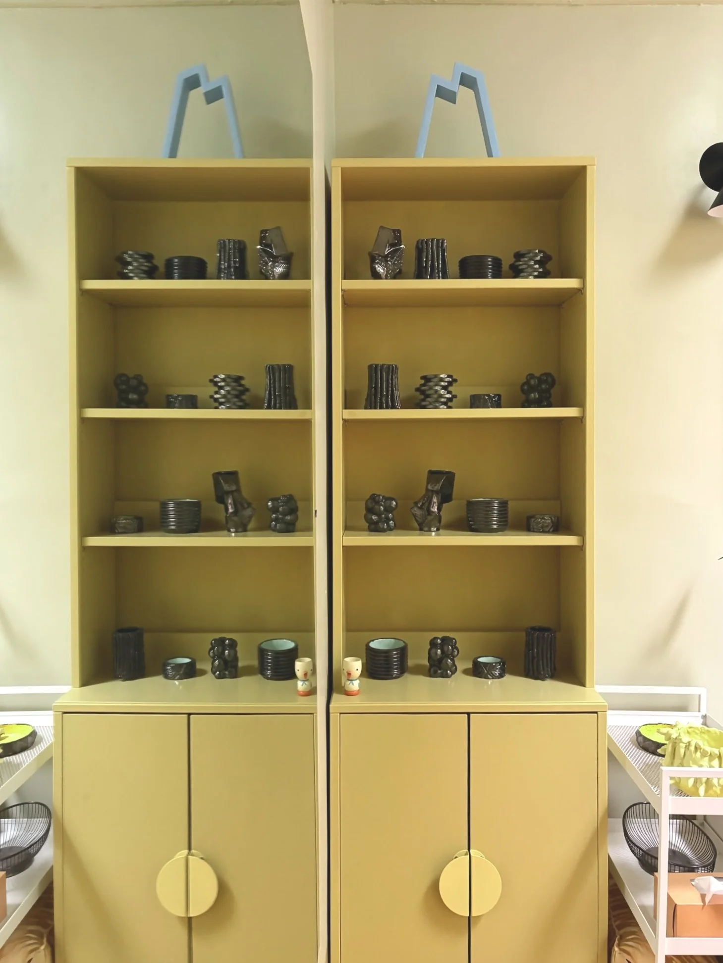 Yellow shelving unit with black ceramic or pottery items and small decorative objects arranged on the shelves and cabinets.