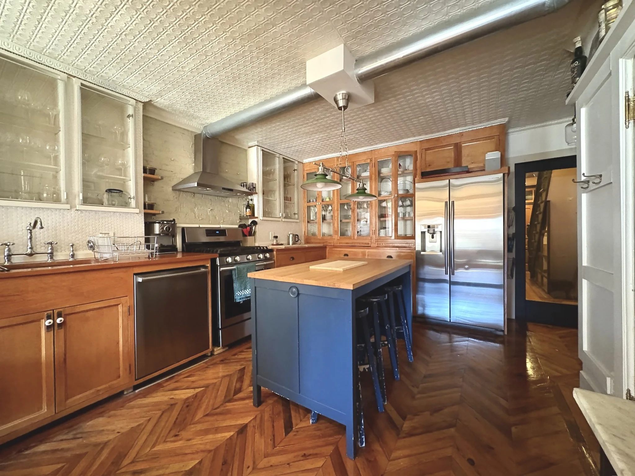 Modern kitchen with wood cabinets, stainless steel appliances, an island with bar stools, and patterned hardwood floors.