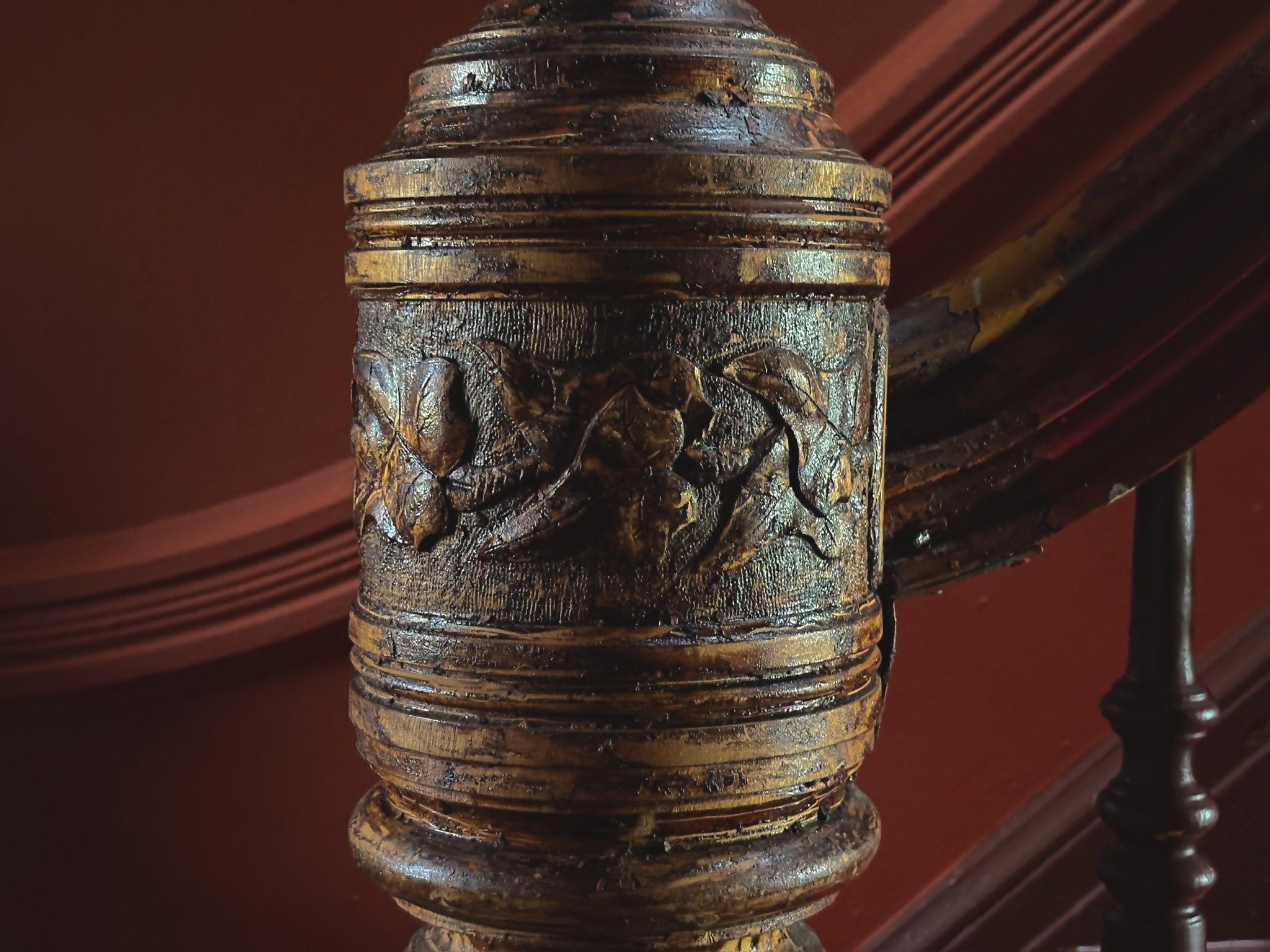 Close-up of an ornate wooden staircase newel post with carved floral details, finished in a glossy brown stain.