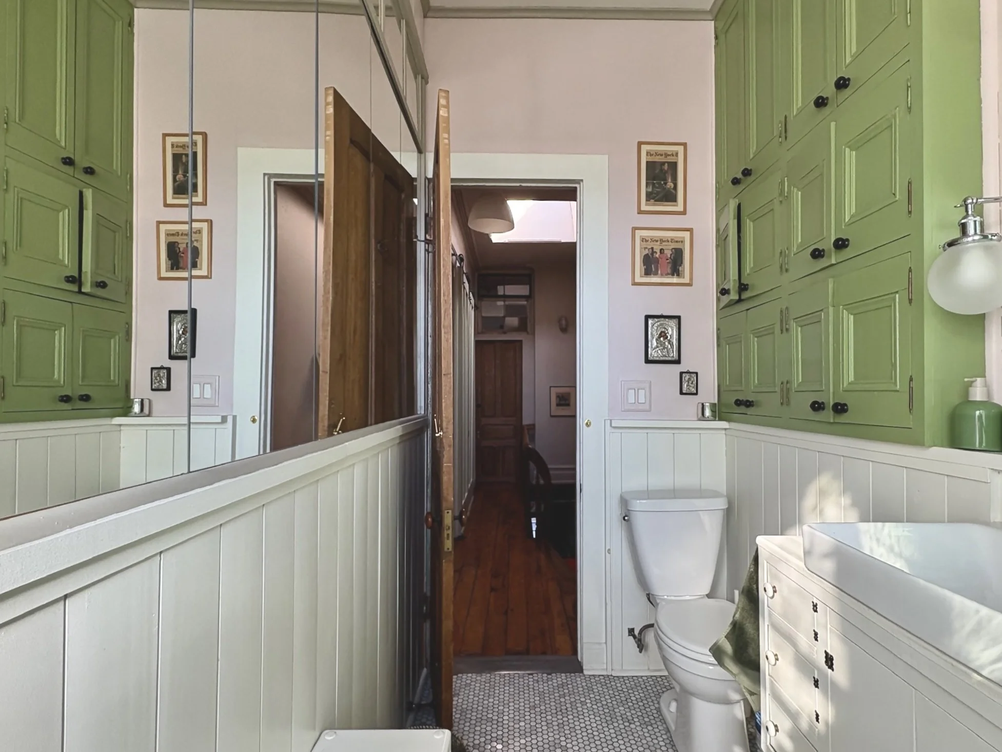 Bathroom with green cabinets, a white toilet, a small white dresser with a vessel sink, and framed artwork on the walls.