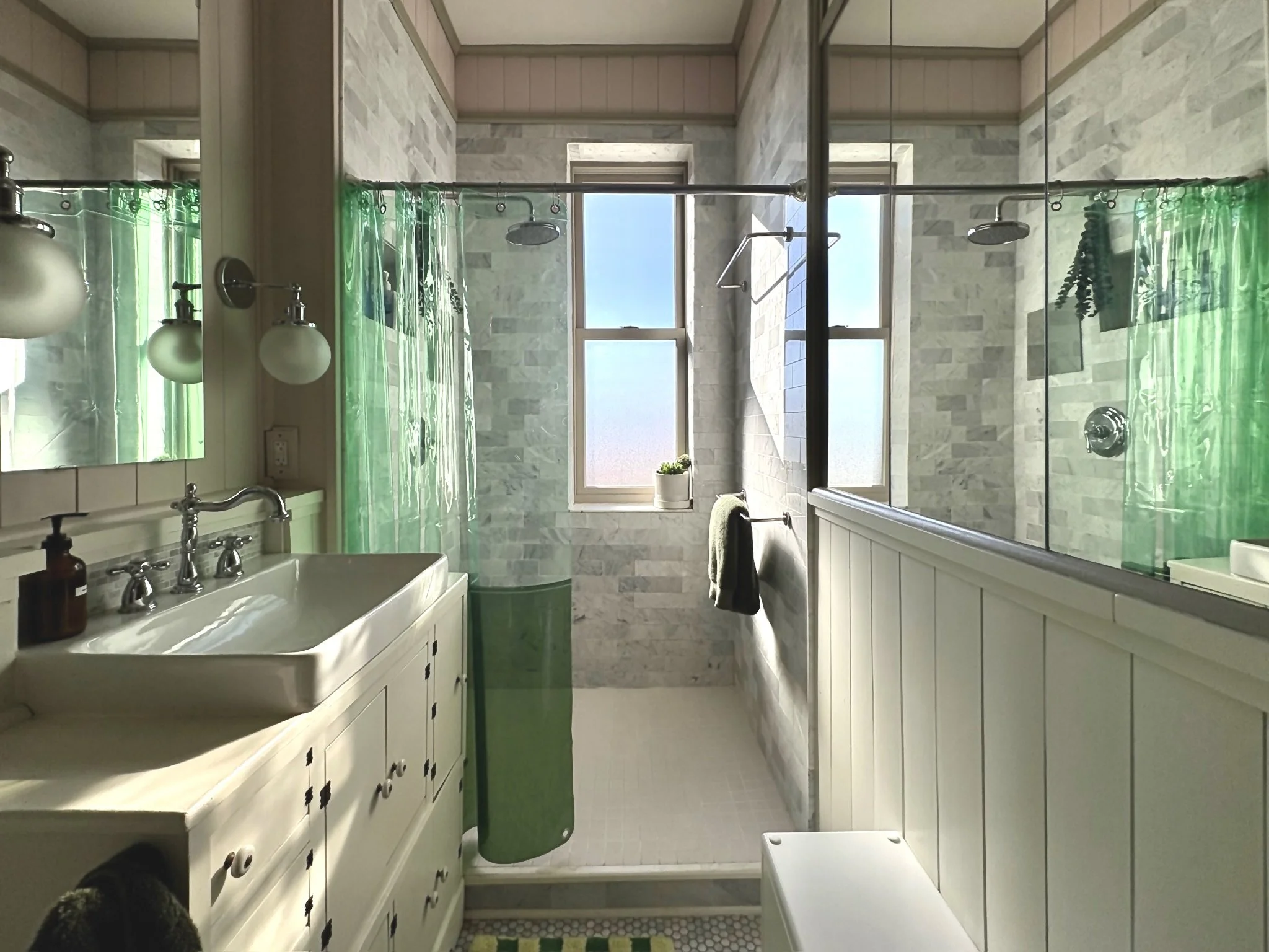 Bright bathroom with a walk-in shower, a large mirror, a white vanity with a sink, green shower curtain, and frosted windows letting in natural light.
