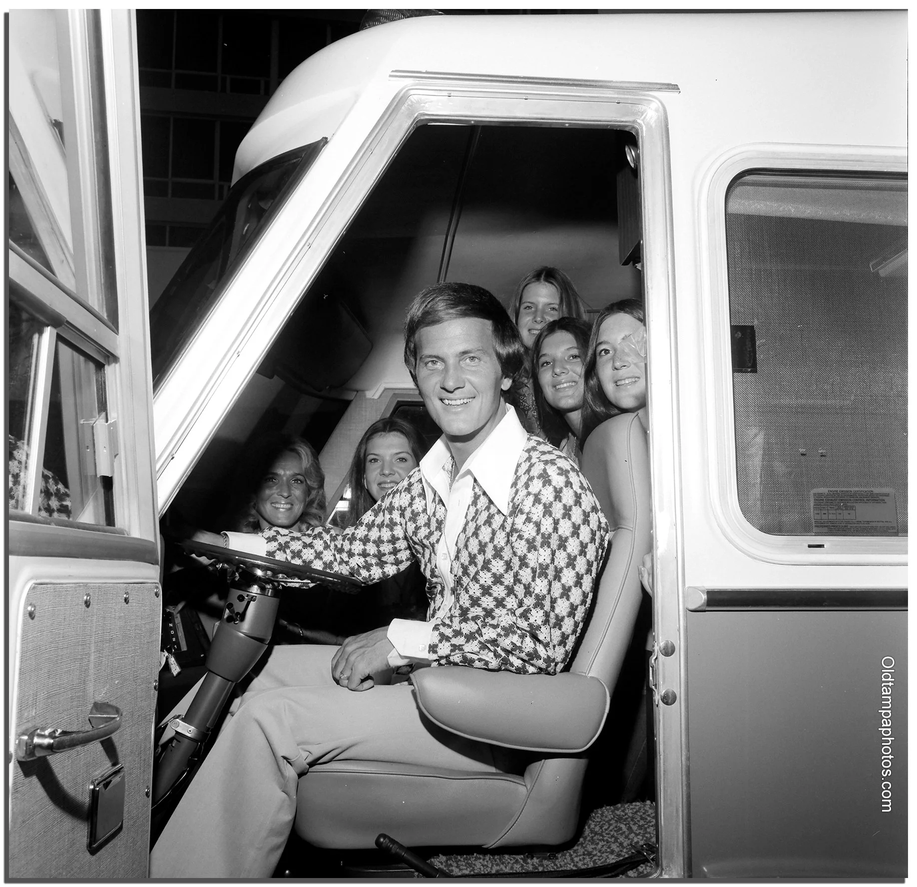 Black and white photo of singer Pat Boone seated in the driver’s seat of a 1970s motorhome with family members inside the RV cockpit.