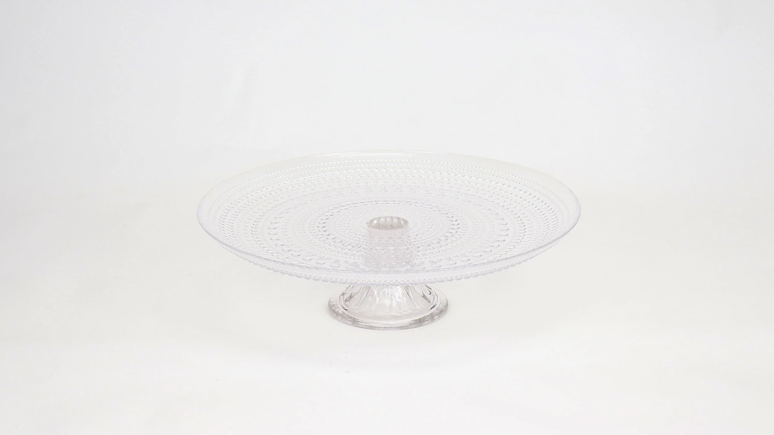 Clear glass cake stand with a textured surface on a white background.