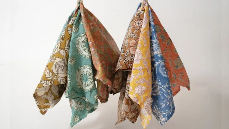 Multiple colorful patterned scarves hanging on hooks against a plain white wall.