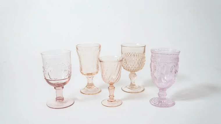 Five vintage pink and purple glass goblets displayed on a white surface against a white background.