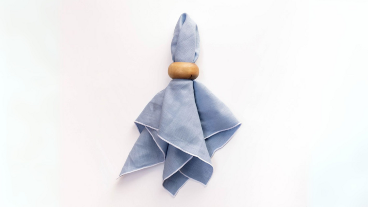 A blue cloth napkin knotted with a wooden ring, hanging against a white background.