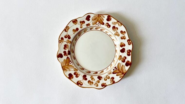 Decorative porcelain saucer with gold floral and leaf patterns on a white background.