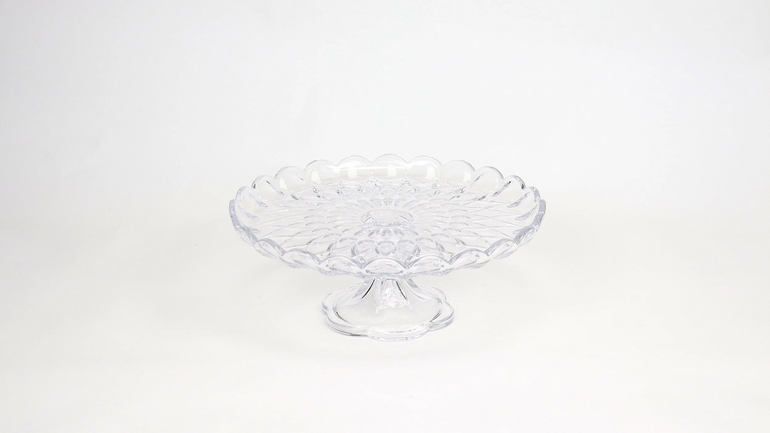 A clear glass decorative cake stand with a floral design, set against a plain white background.